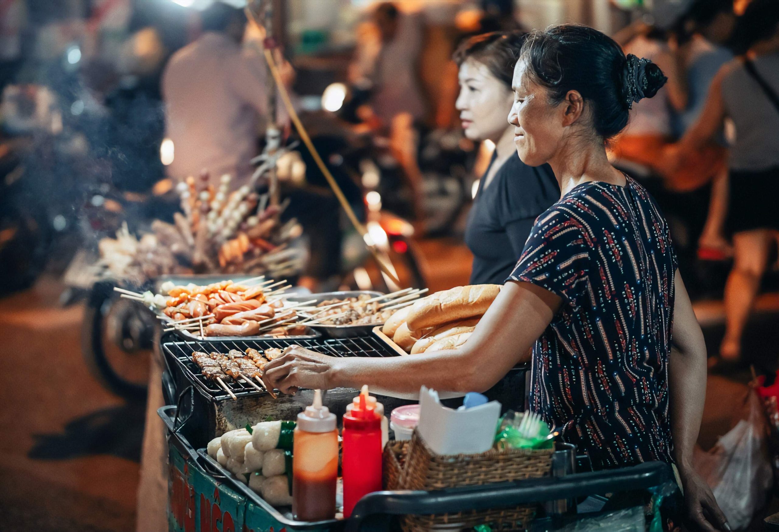 Two women selling grilled street food.