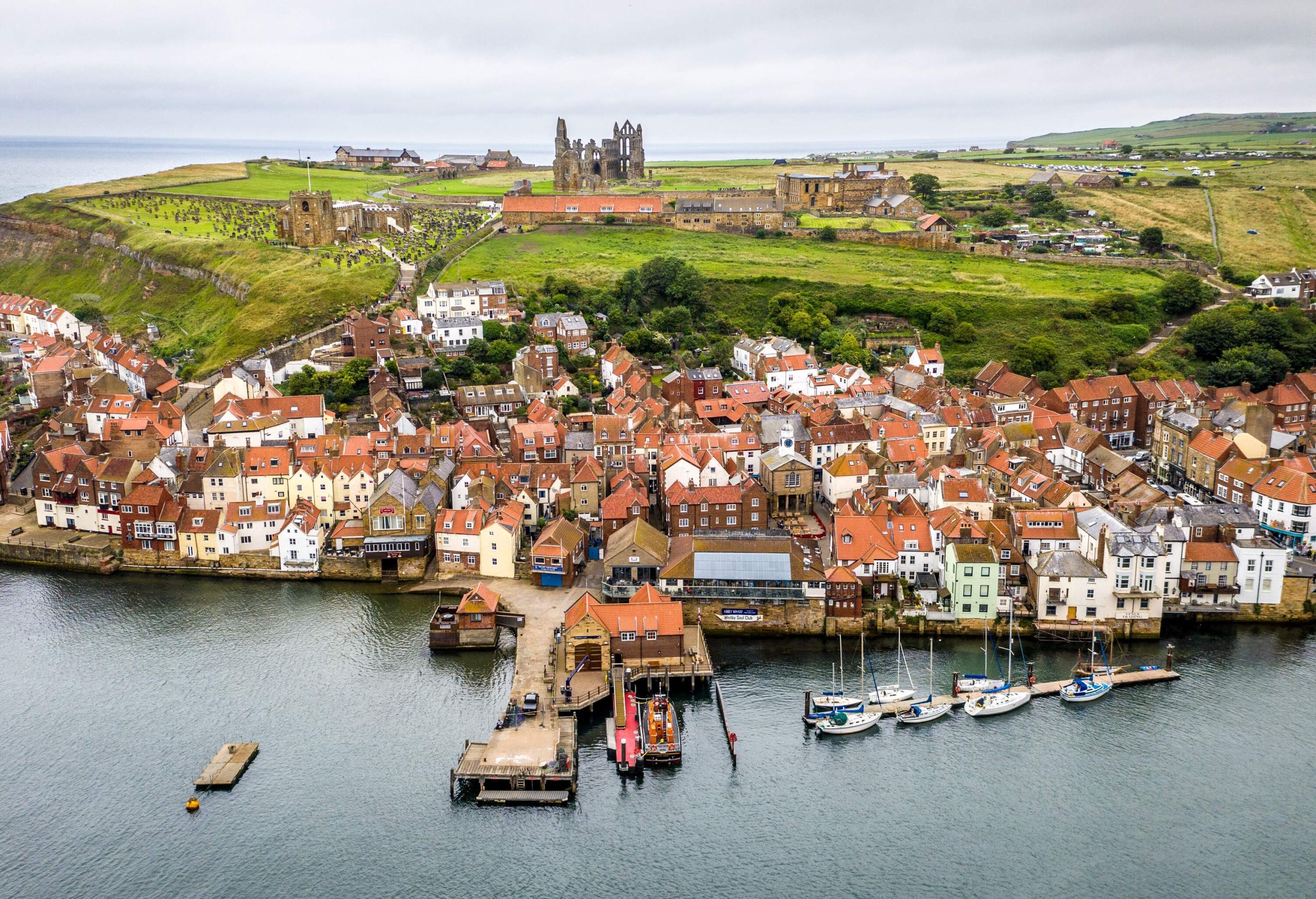 A coastal town with buildings perched on a hillside with a ruined castle on top of a hill.