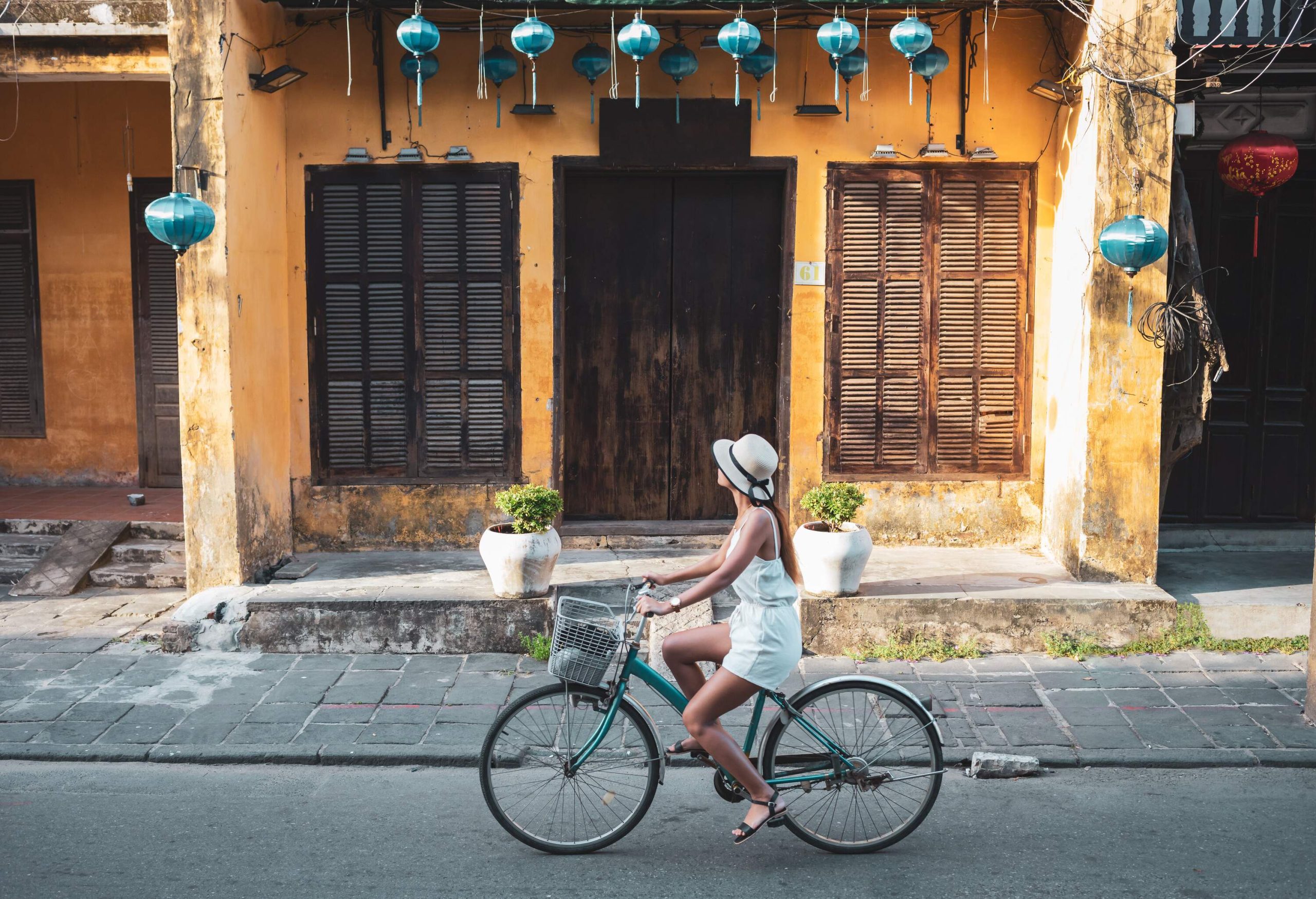 A woman tourist leisurely cycles through the charming old district, with a row of faded-paint houses in the background.