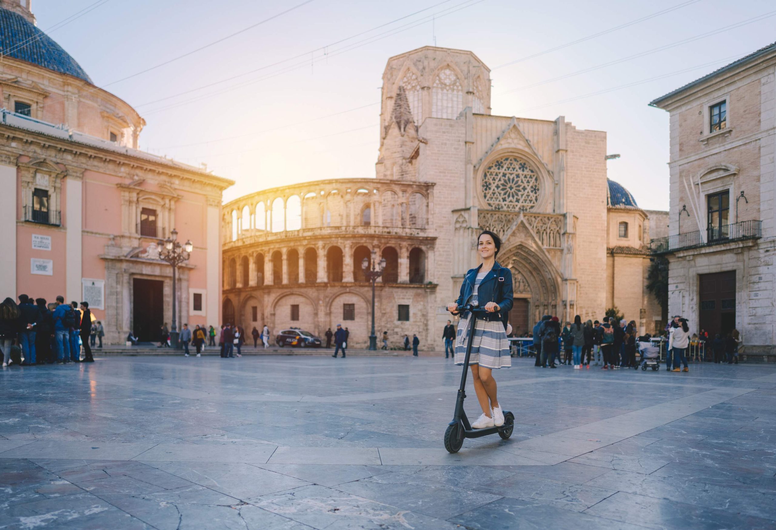 A woman on a scooter in a plaza square surrounded by classic historical buildings.