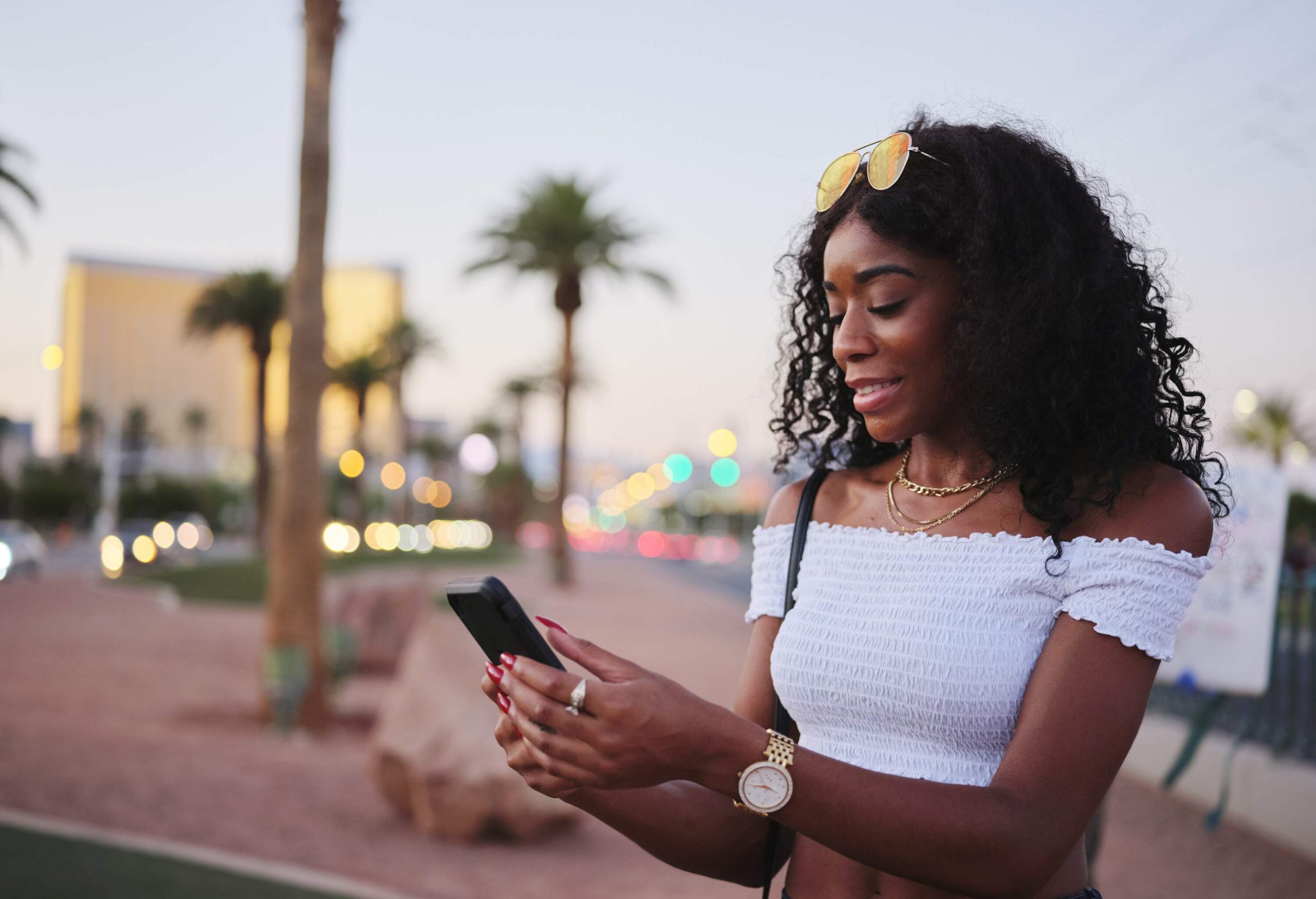 A woman in a white off-shoulder top using her phone as she stands along a promenade. 