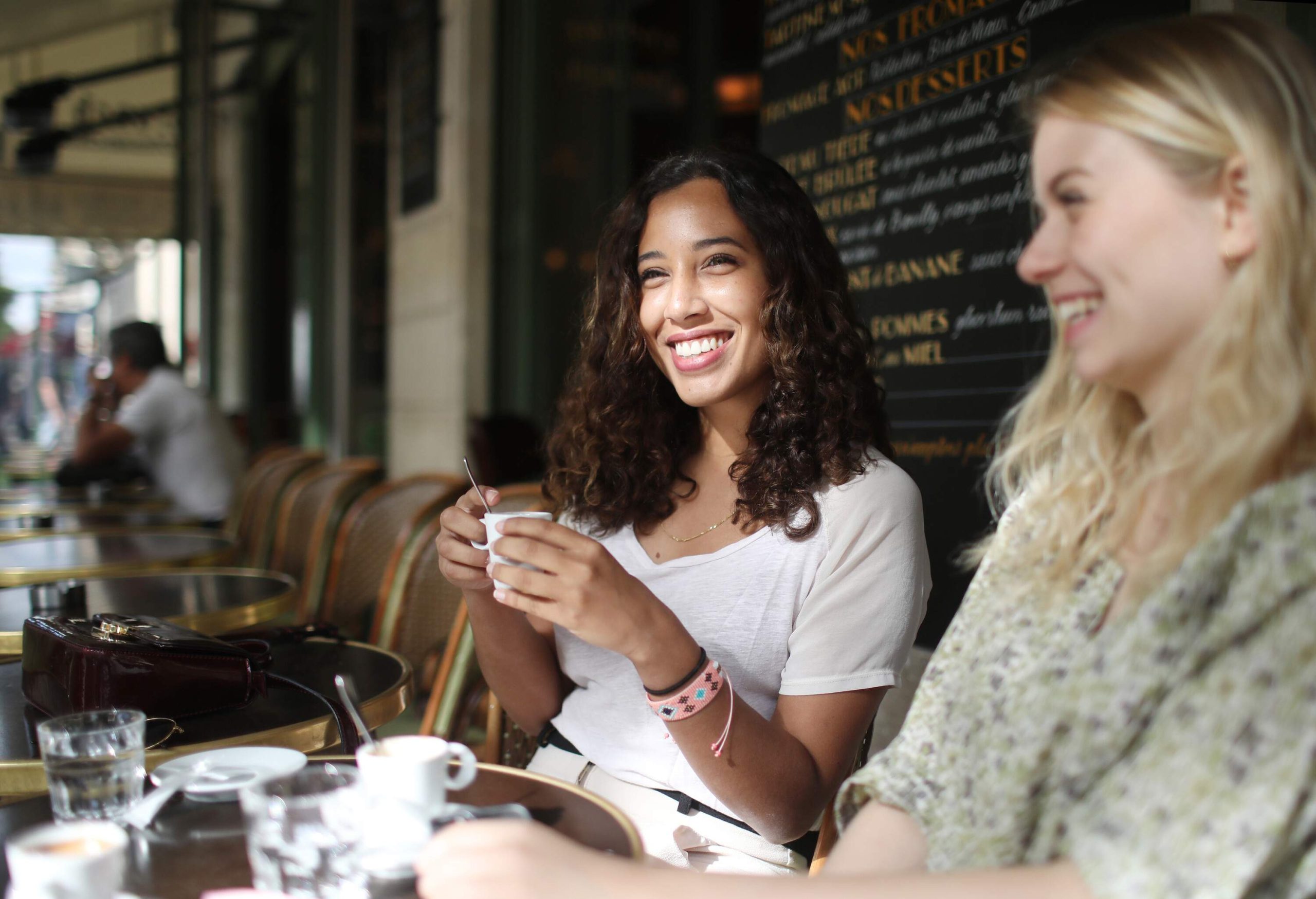 Two happy women sit outside a coffee shop.