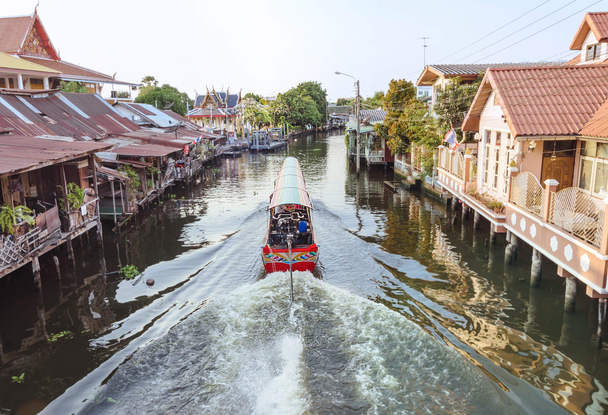 A red passenger boat cruises across a canal amid houses perched overwater.