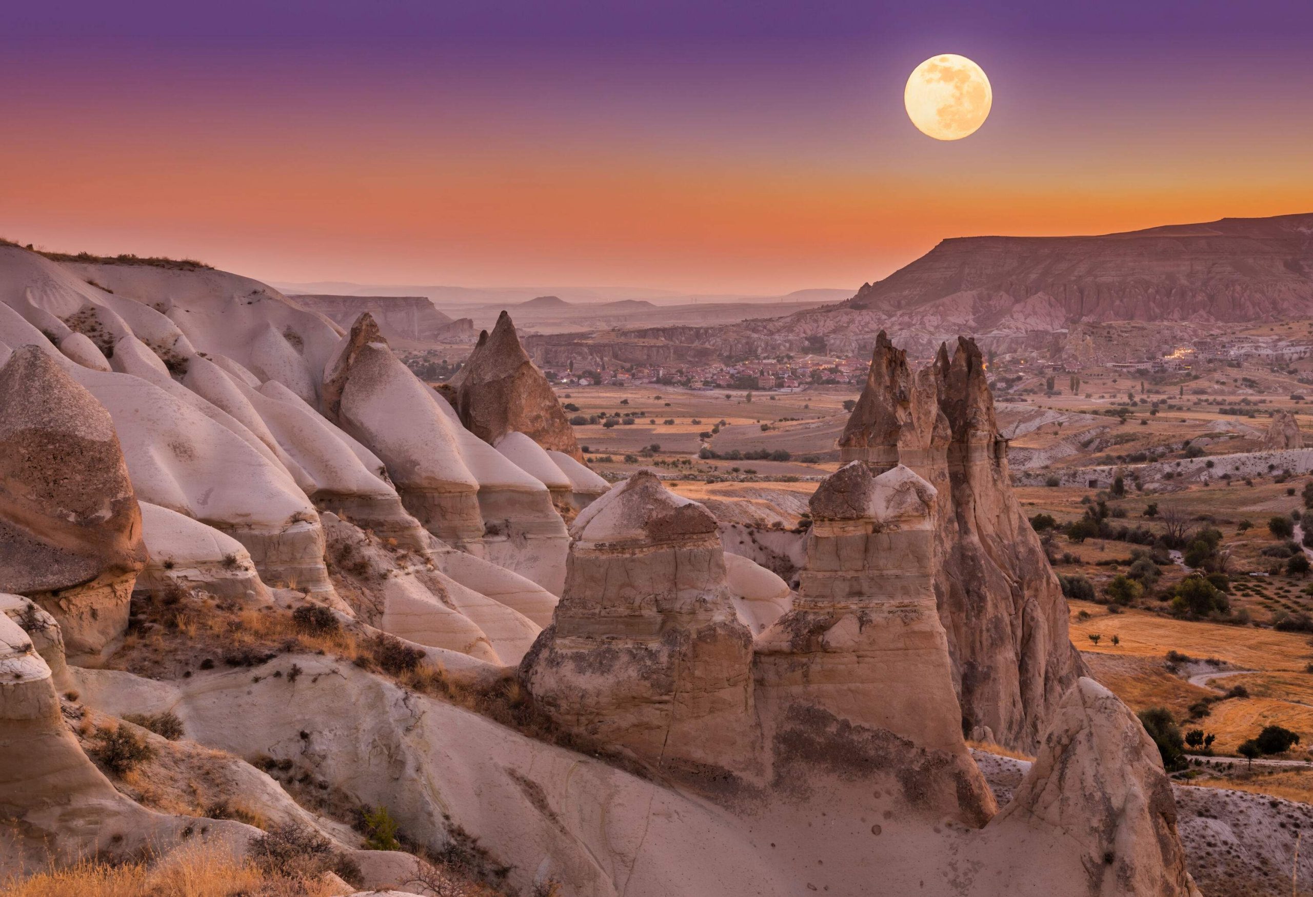 The scenic full moon shines above the cliff on the valley with unusual rock formations.