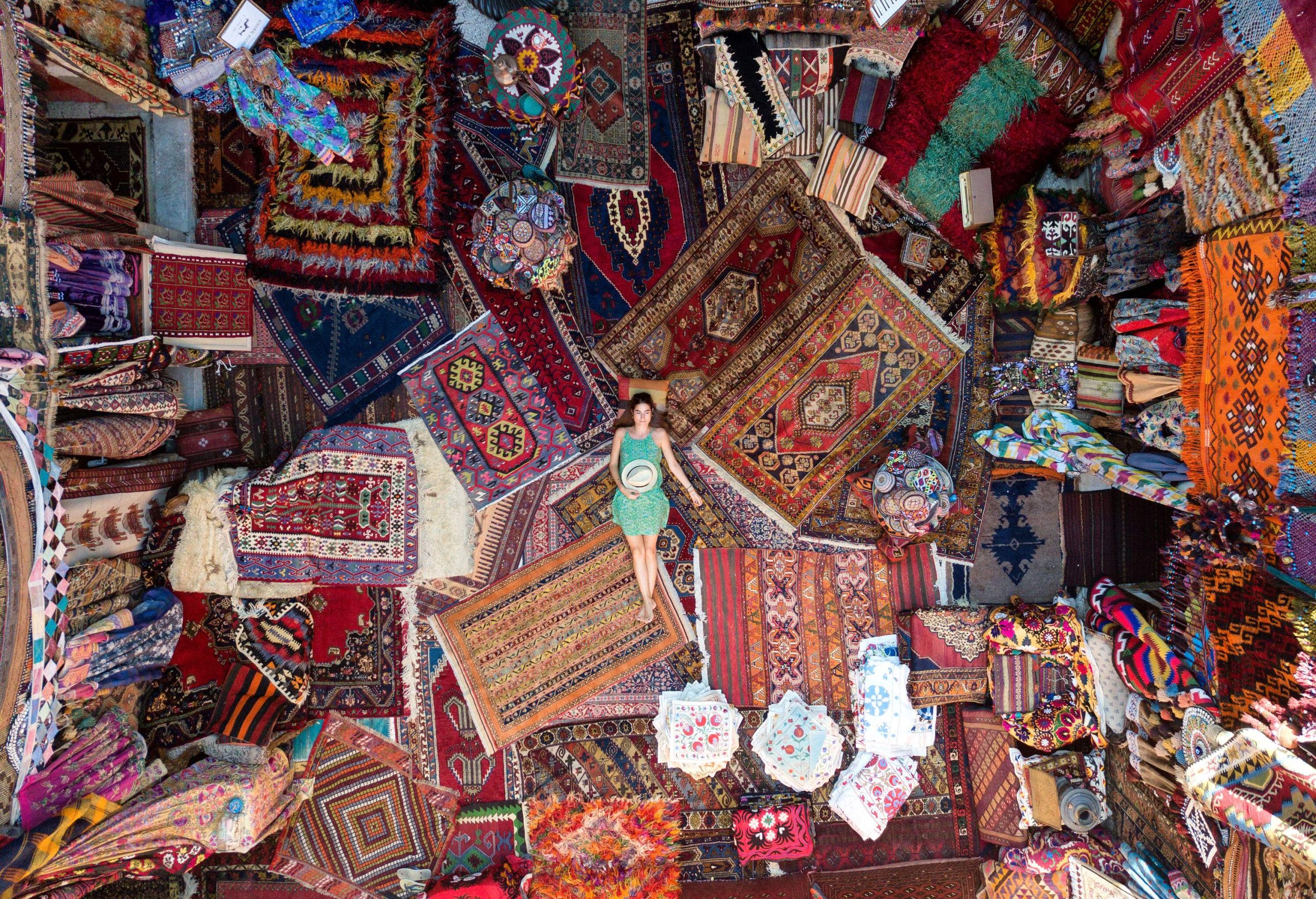 A person lies comfortably on a variety of intricately woven carpets within a vibrant carpet store.