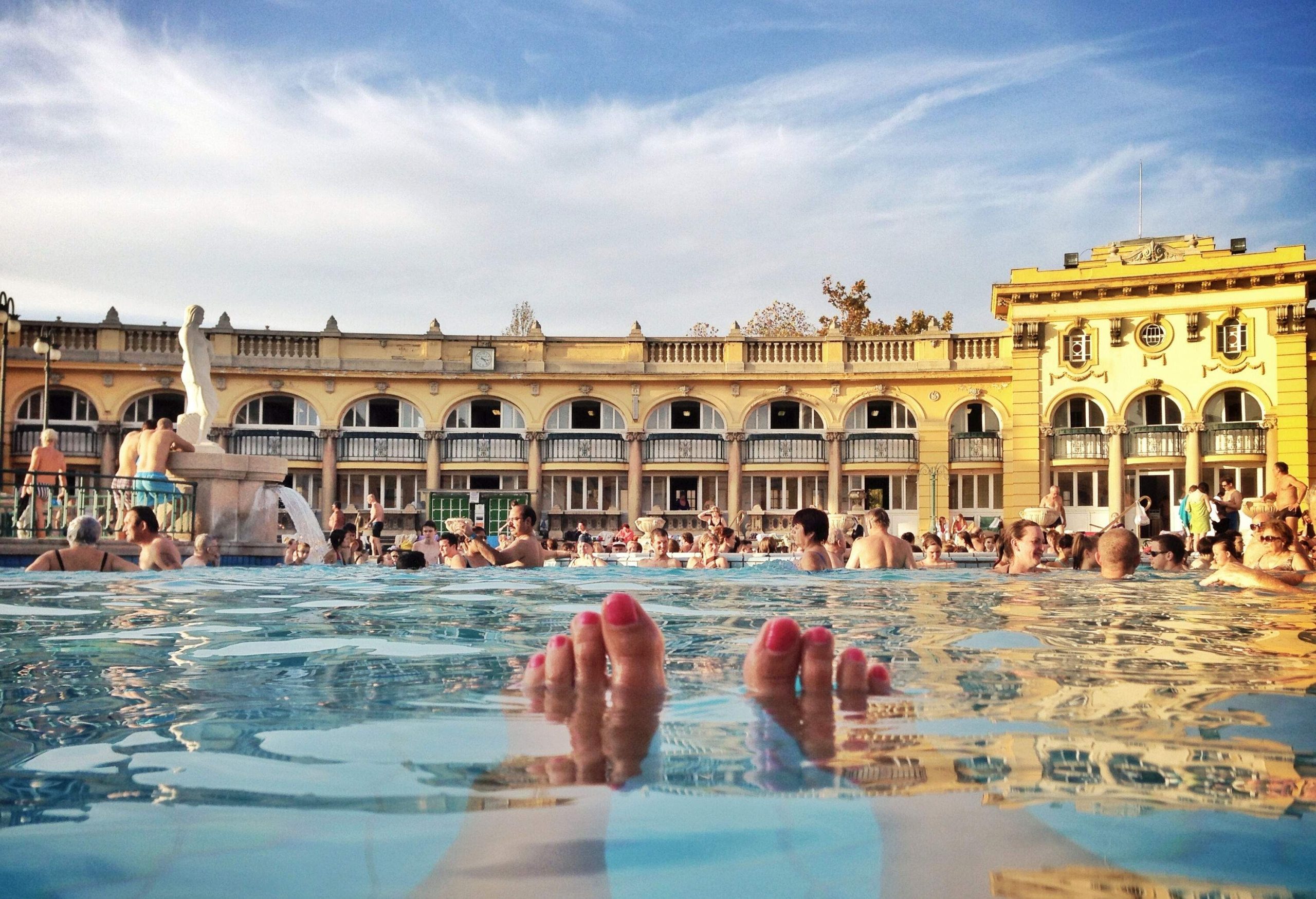 A dense pool in a traditional thermal bath in a neo-baroque building with yellow facades and arched doors and windows.