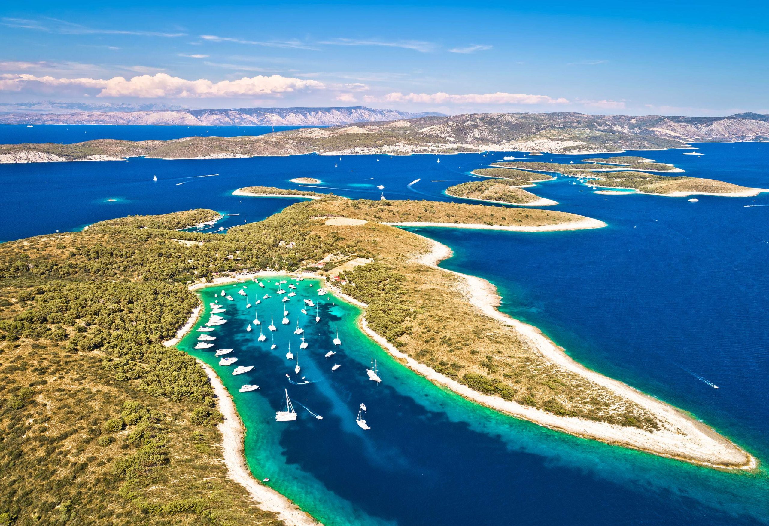 Boats sailing through the deep blue waters of a narrow cove surrounded by forested islands.