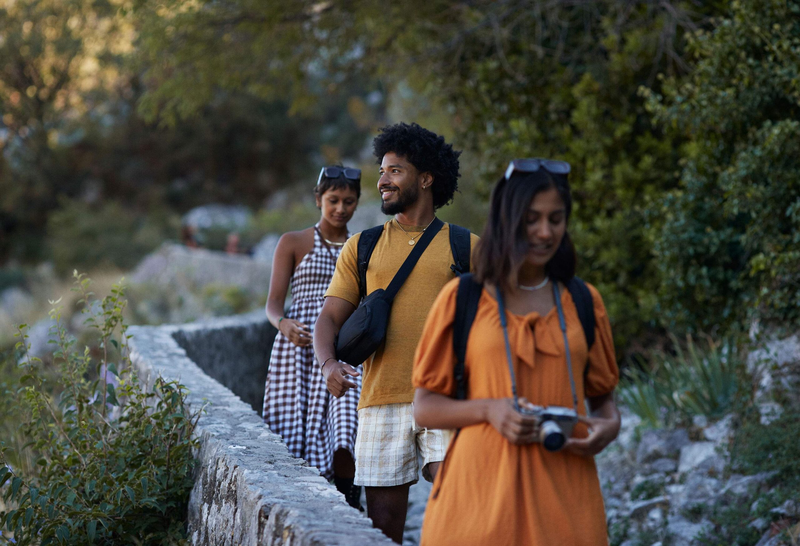 A smiling young man hiking down a mountain with his female friends during a vacation with the sun sets in the background.