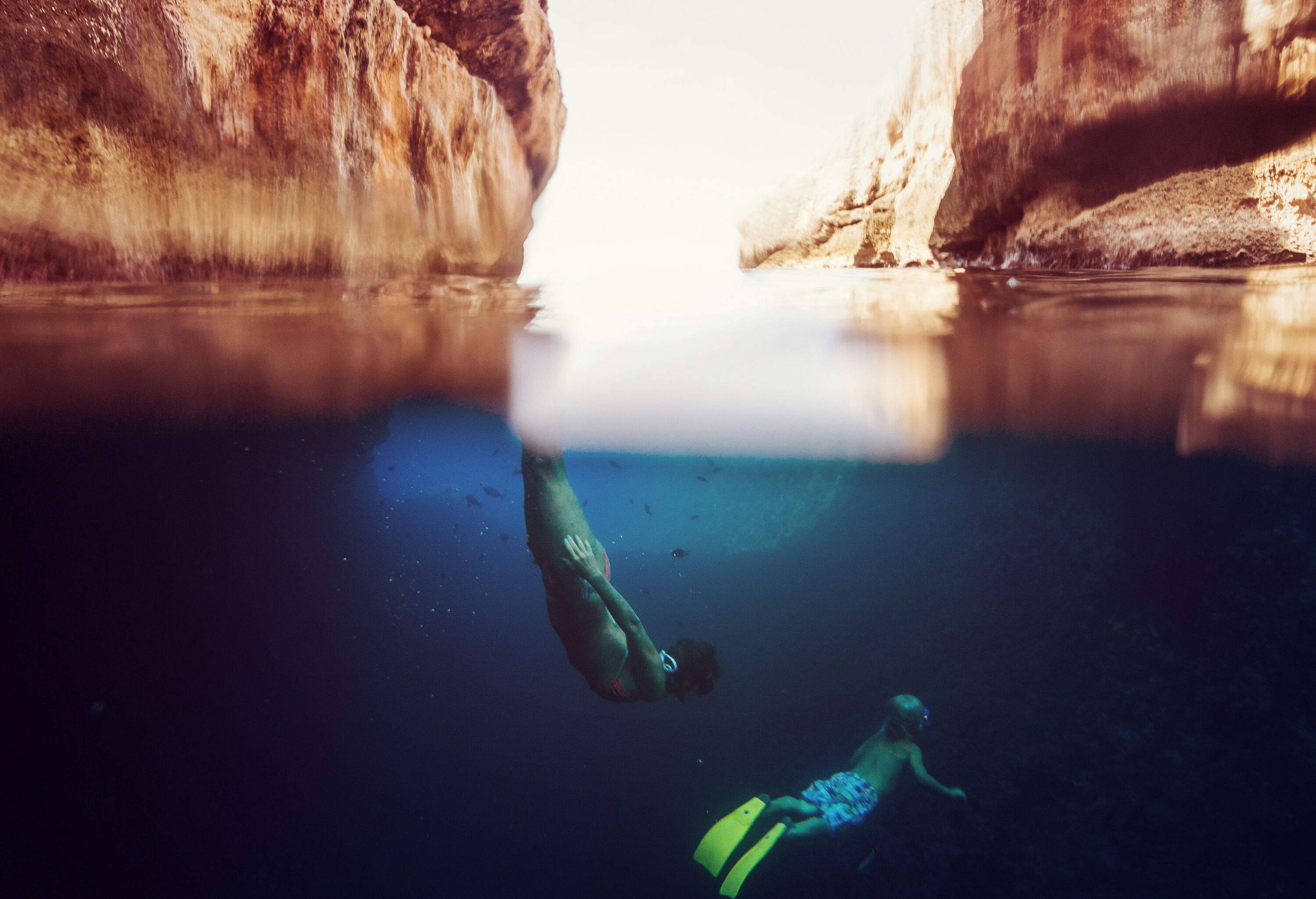 A mother and son are under the water with a view of two rock cliffs.