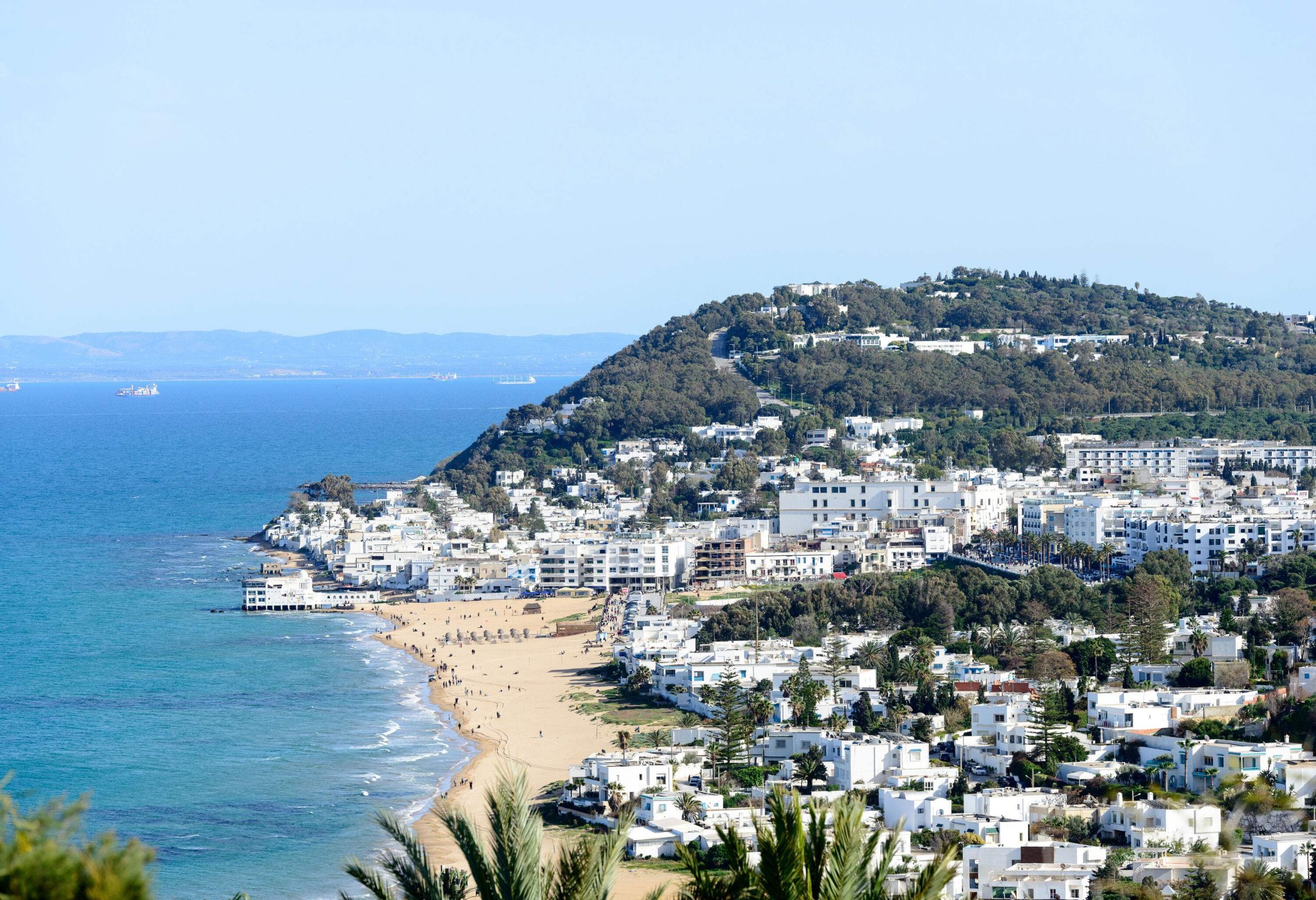 A white sand beach with whitewashed buildings along the coast and hills.