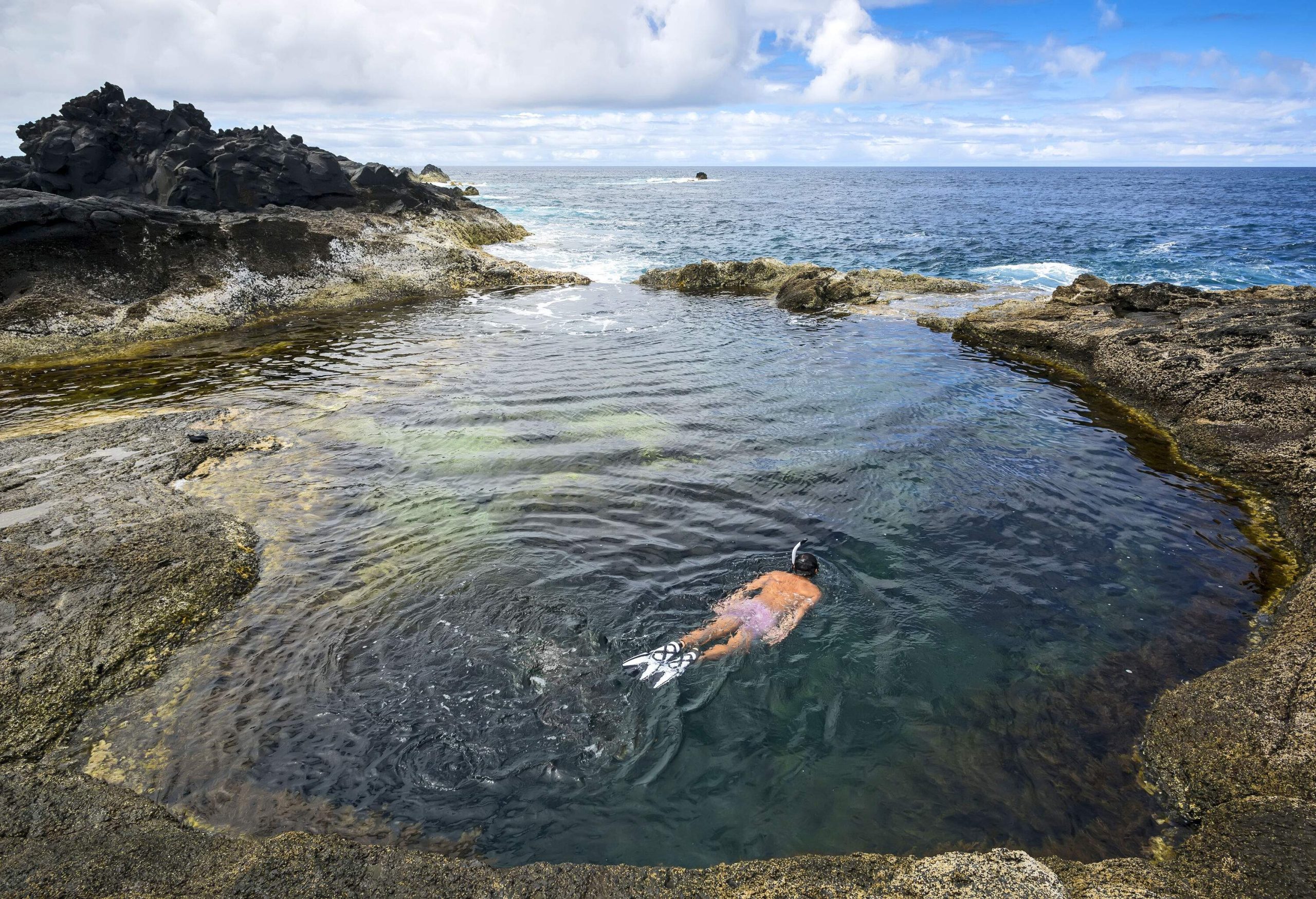 A man wearing a snorkel mask and fins swimming in a natural rock pool at the seaside.