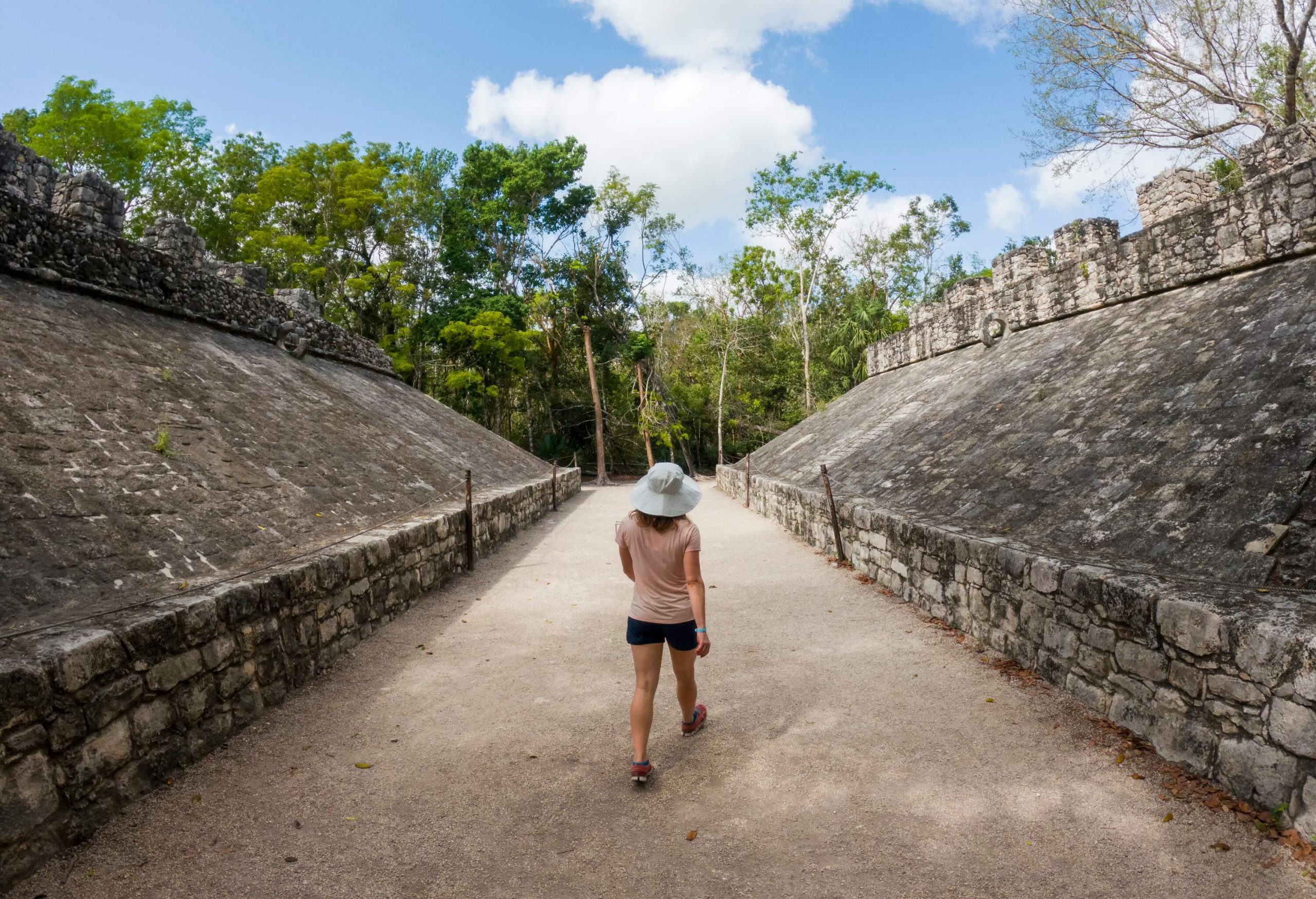 Back view of a young girl walking between the rock ruins surrounded by trees in a Mayan archaeological area.