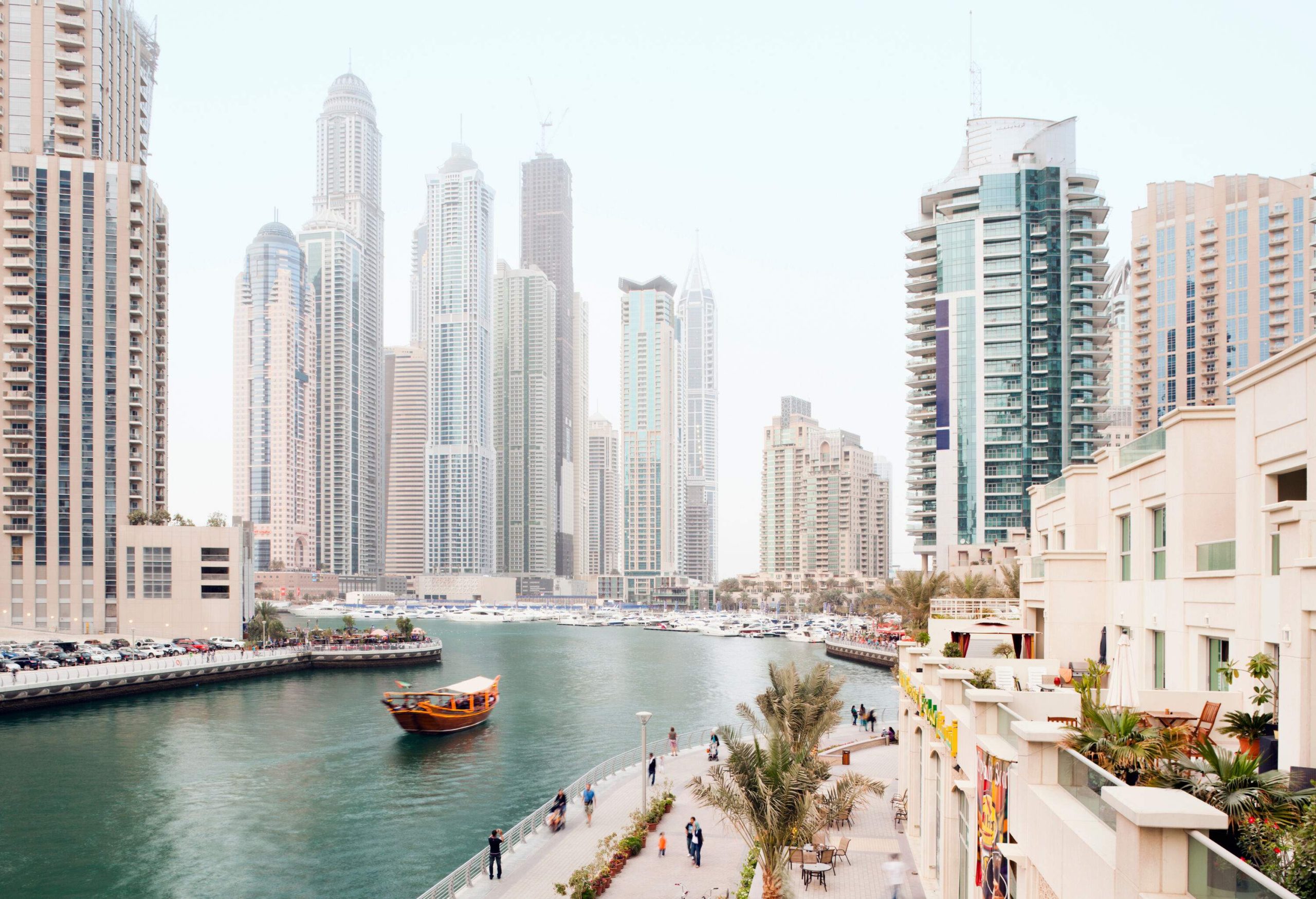 The affluent Dubai Marina skyline with canal-side promenades lined with restaurants and high-rise buildings.