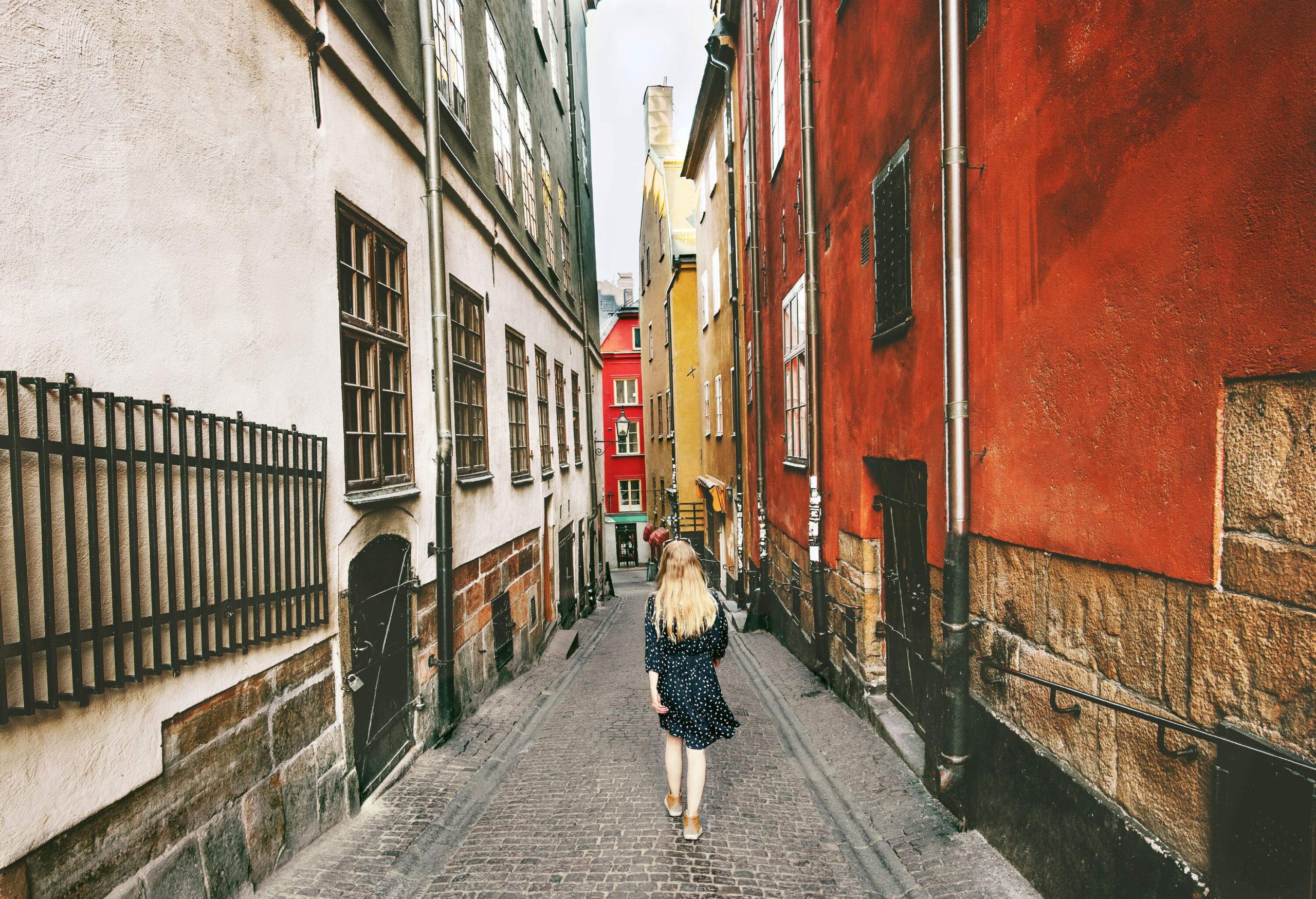 A person on a narrow cobbled street lined with tall and colourful buildings.