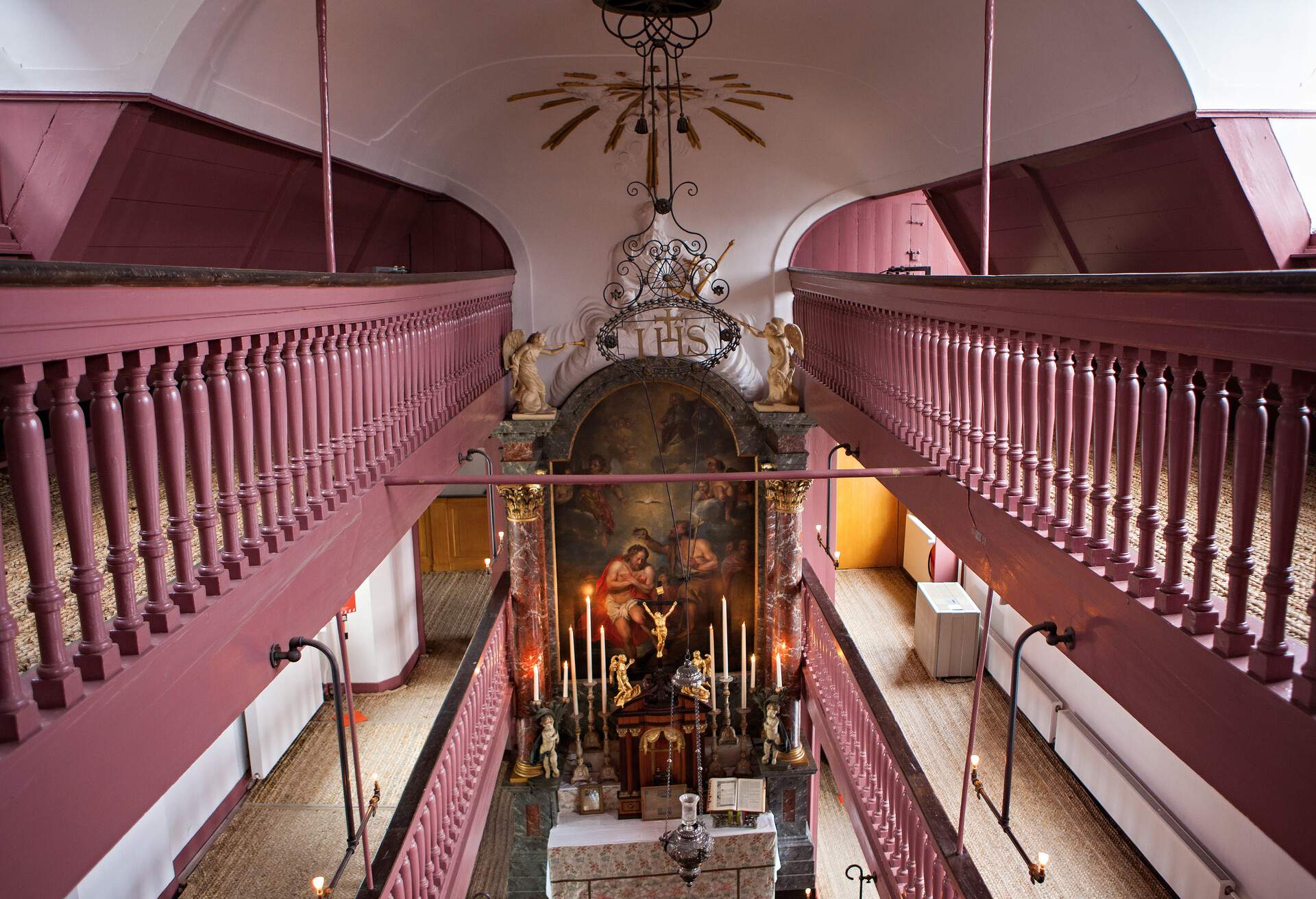 a small and narrow church room with an alter in the middle and a pink-colored railing 