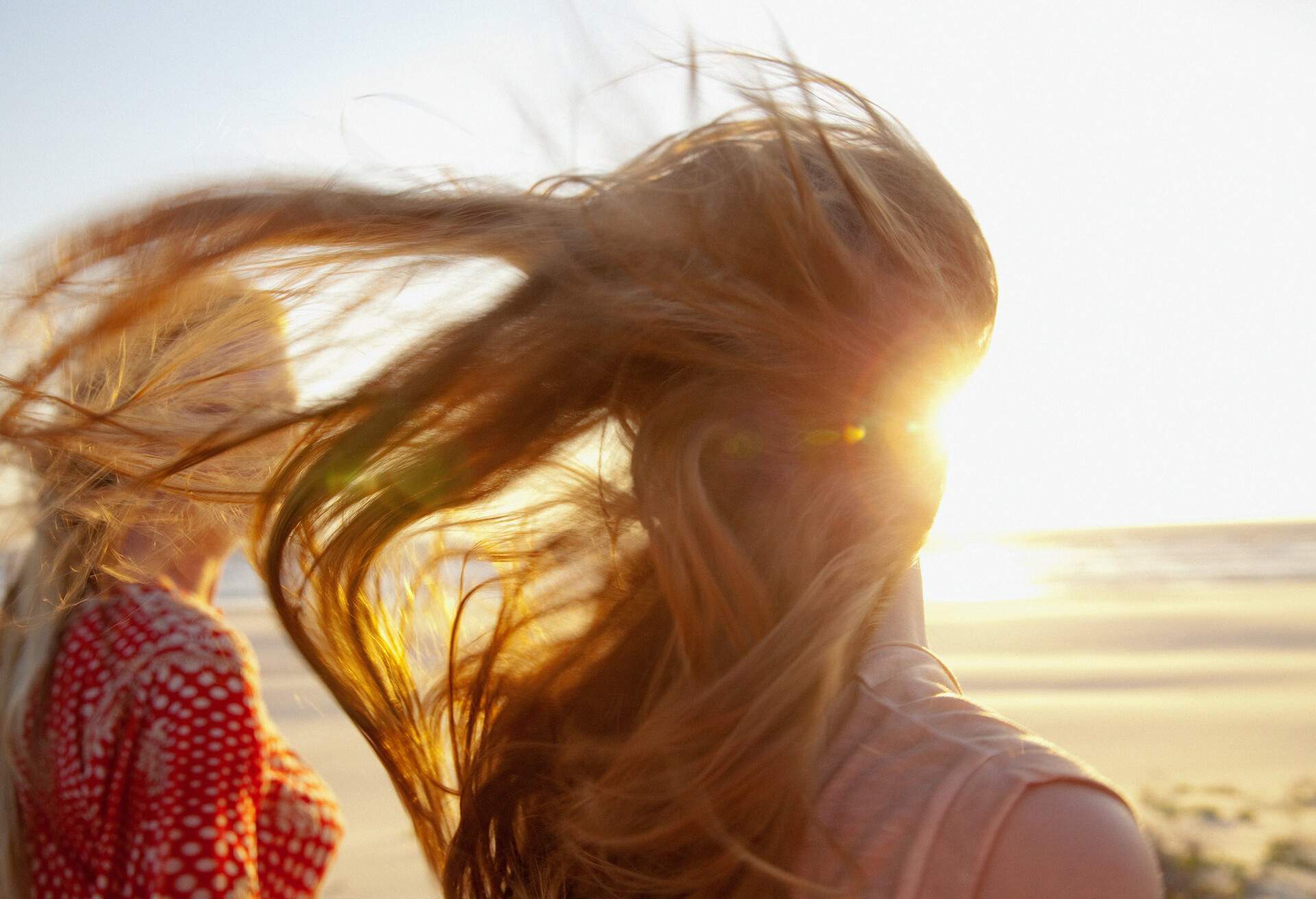 A woman's golden hair being tossed by the breeze as she stands next to another woman on the beach.