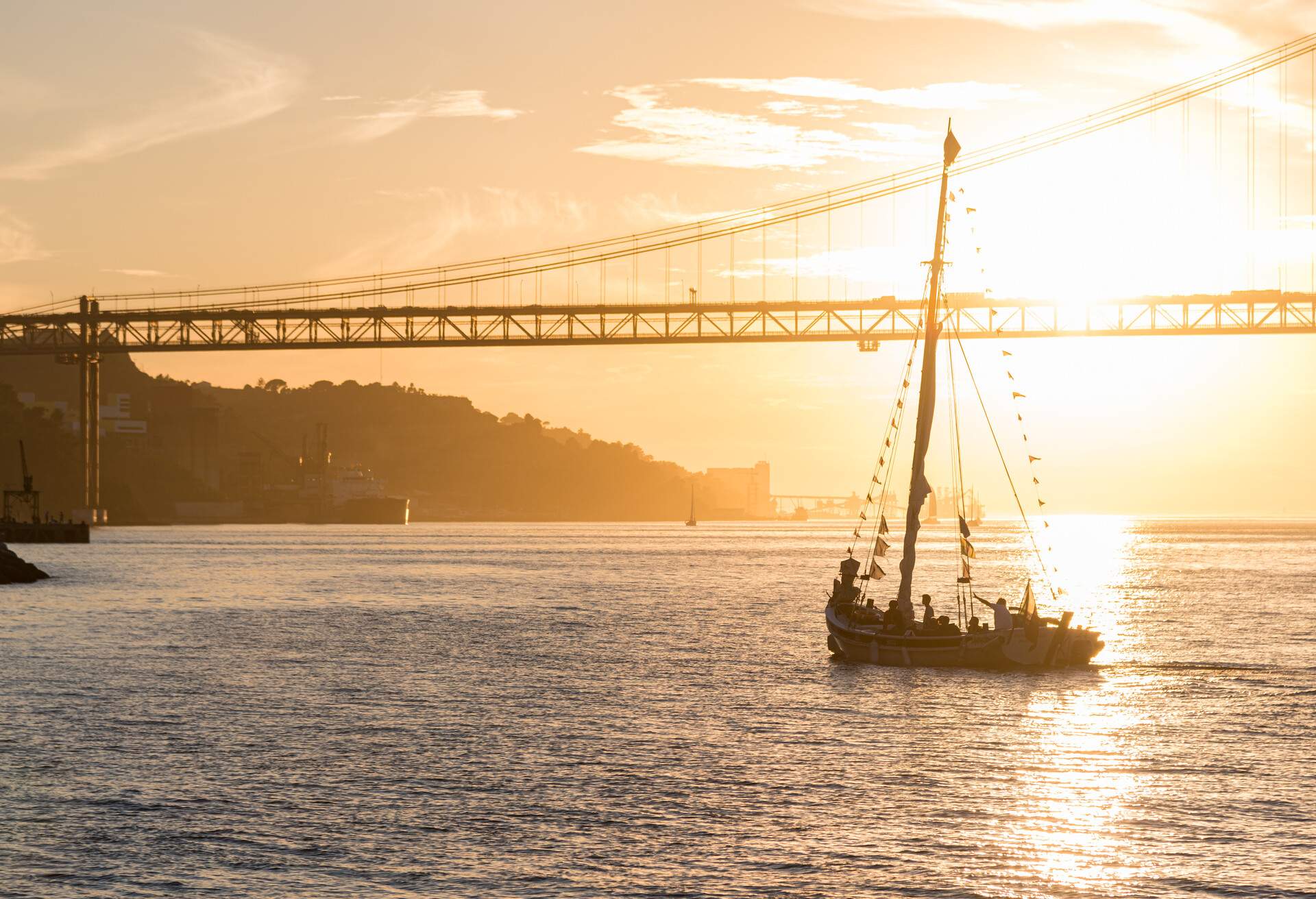 A ship sailing across a river spanned by a suspension bridge at sunset.