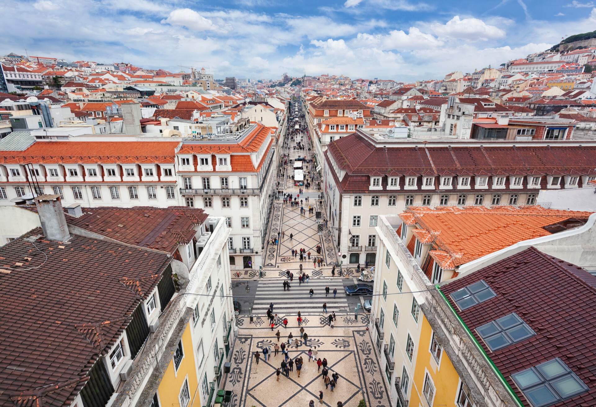 People walk in the famous pedestrian street "Rua Augusta," with mosaic pavements lined with several stores and cafes in the middle of compact buildings.