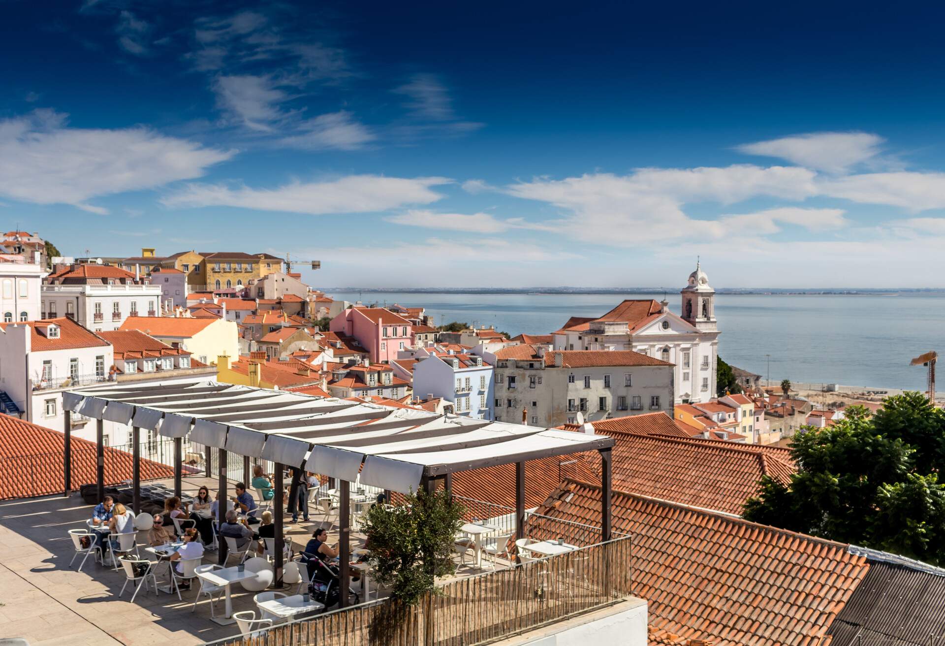 People dining on a terrace overlooking the city rooftops and the sea.