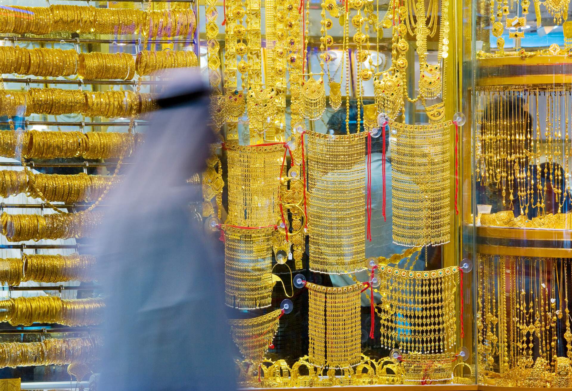 A variety of intricate gold jewelry pieces hanging from a glass window.