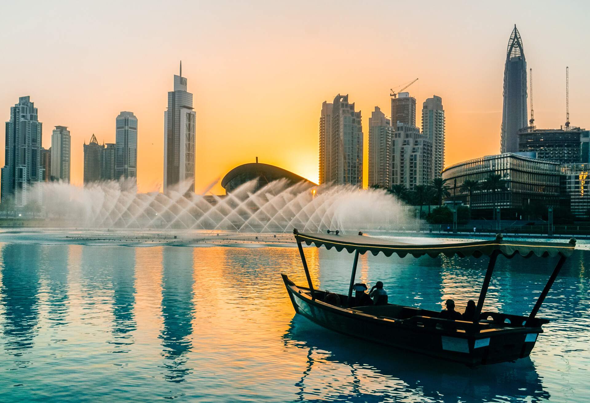 People on a boat contemplate the fountains of the lake and the cityscape with modern and stylish skyscrapers against the twilight sky.