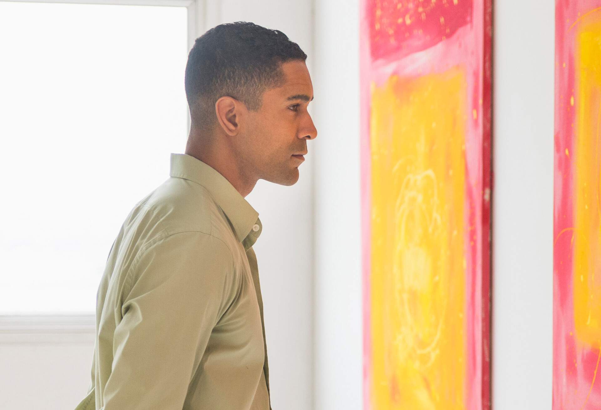 A man in a long-sleeve shirt stares at an abstract art on the wall.