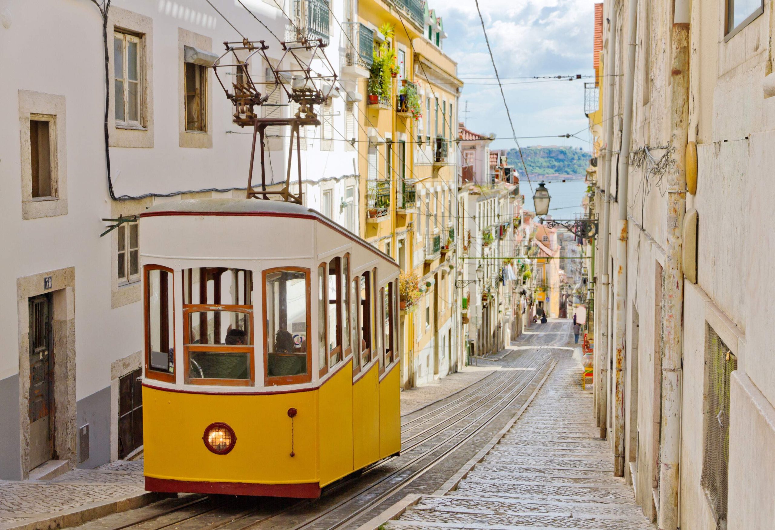 A yellow tram climbs the hill between colourful houses.