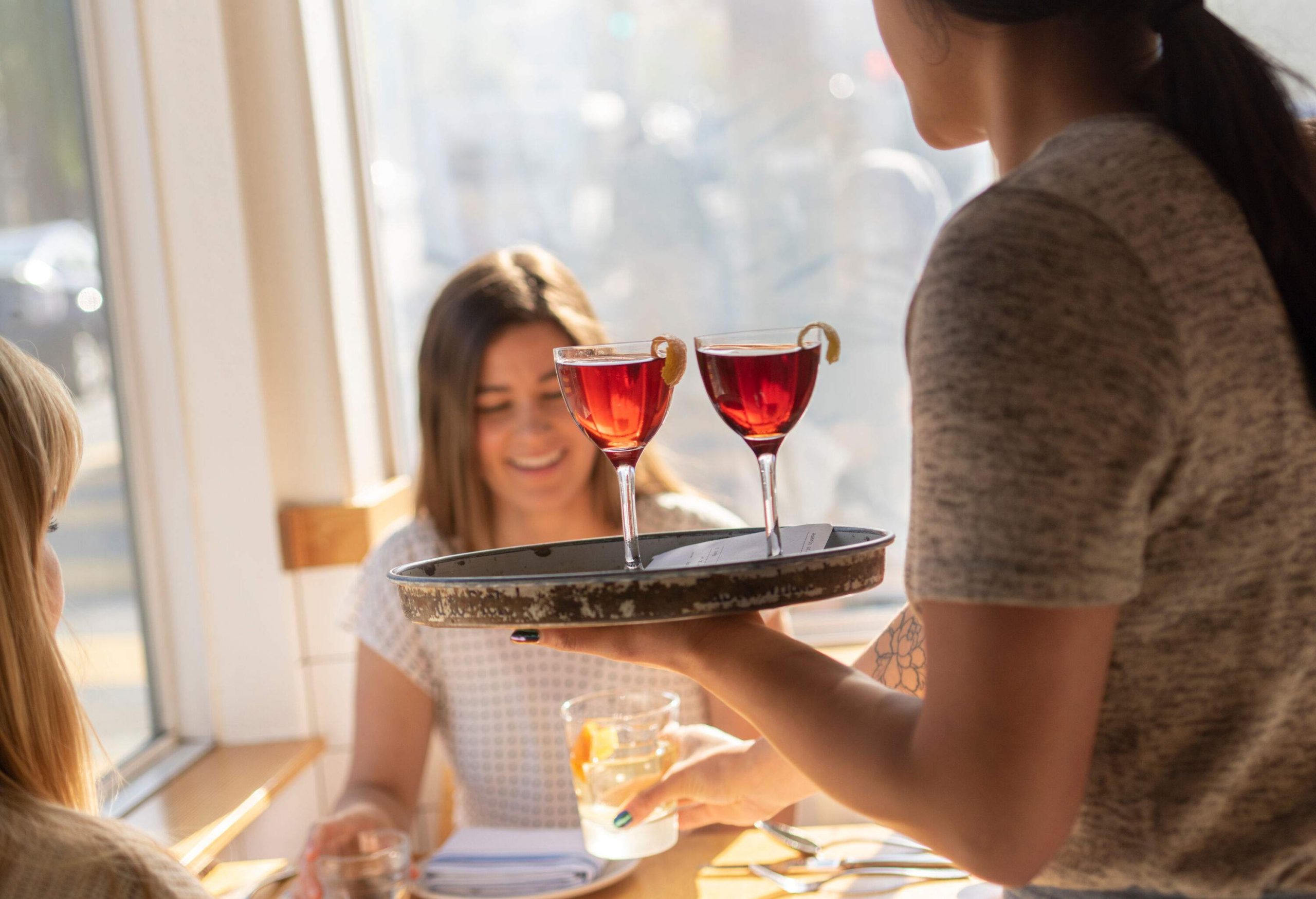 A friendly server gracefully serves beverages to patrons, their faces adorned with bright smiles.