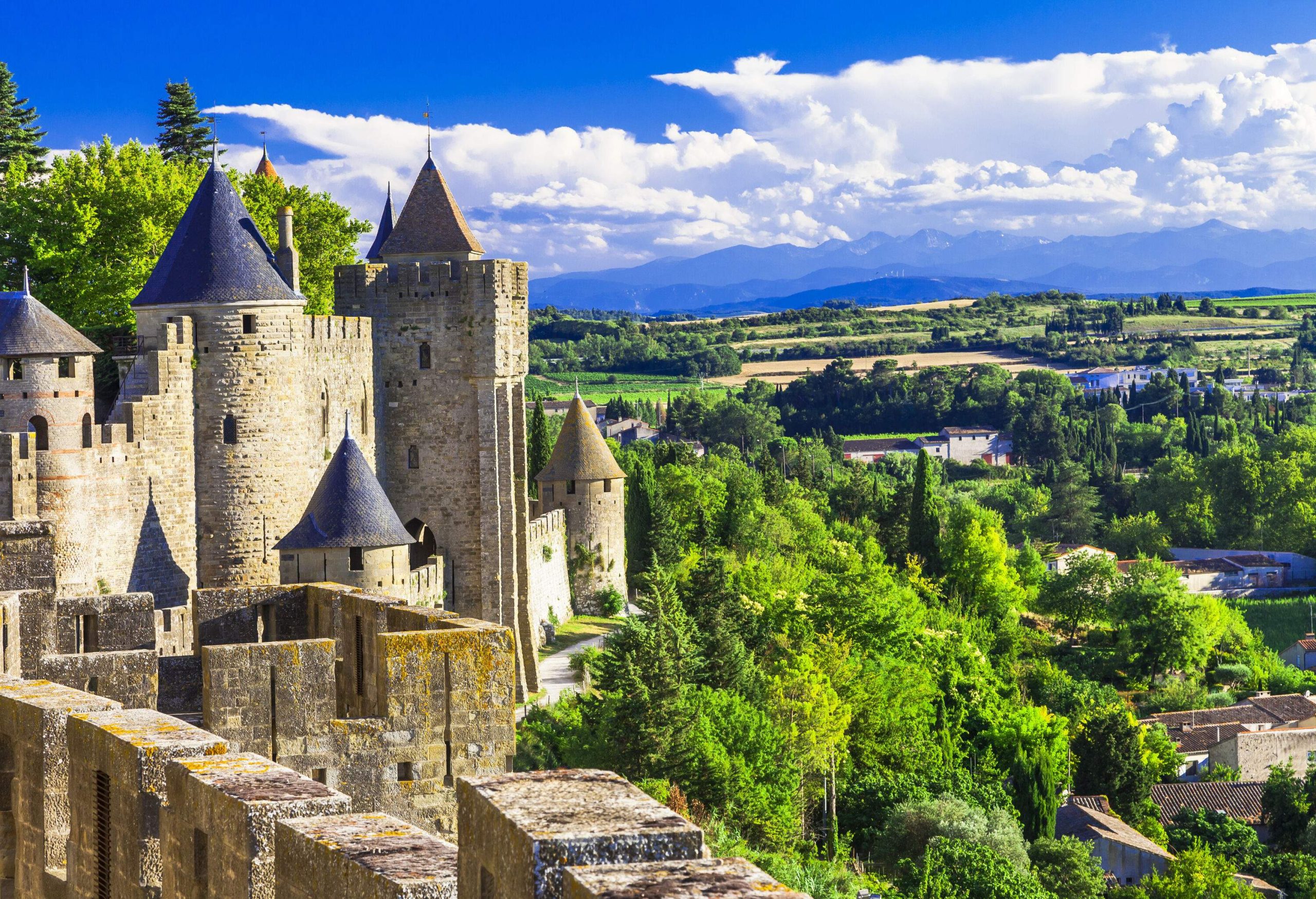 A portion of the outer wall of a medieval citadel lies on a lush forested hill.