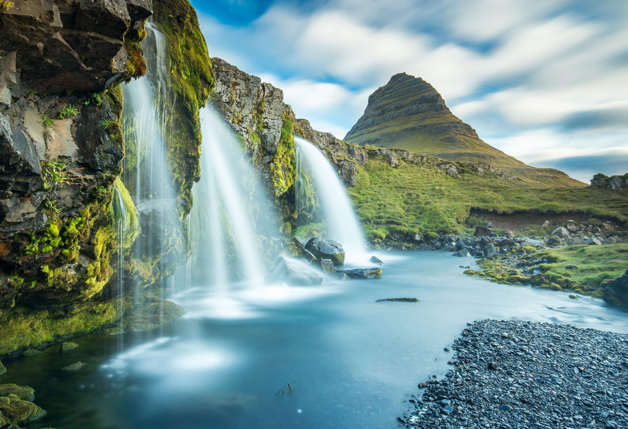 A picturesque waterfall from a lush and rugged cliff down to a shallow river.