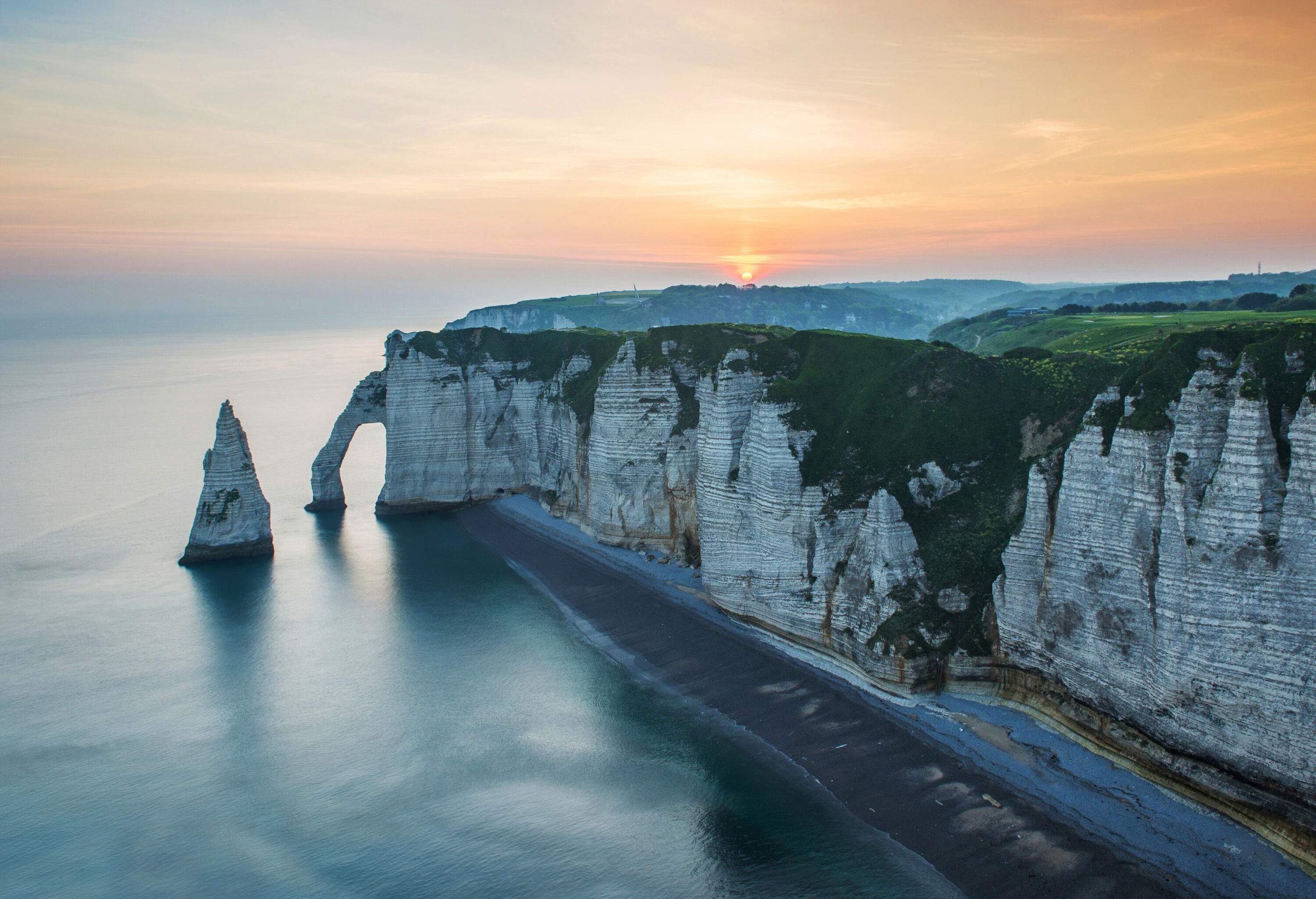 A chalk cliff with an arch along the beach at sunset.