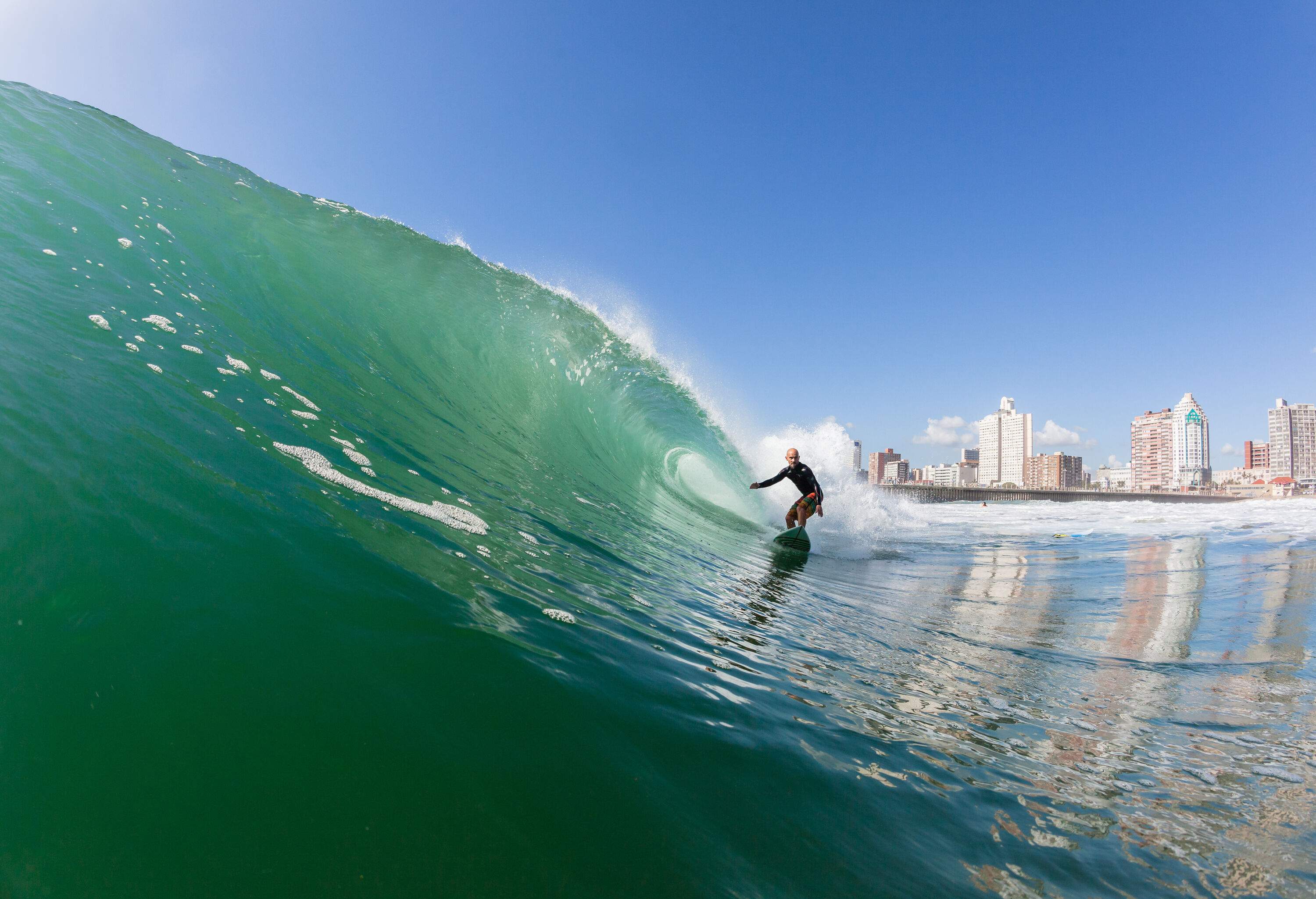 A surfer skillfully rides an ocean wave against the backdrop of modern tall buildings on the coast.