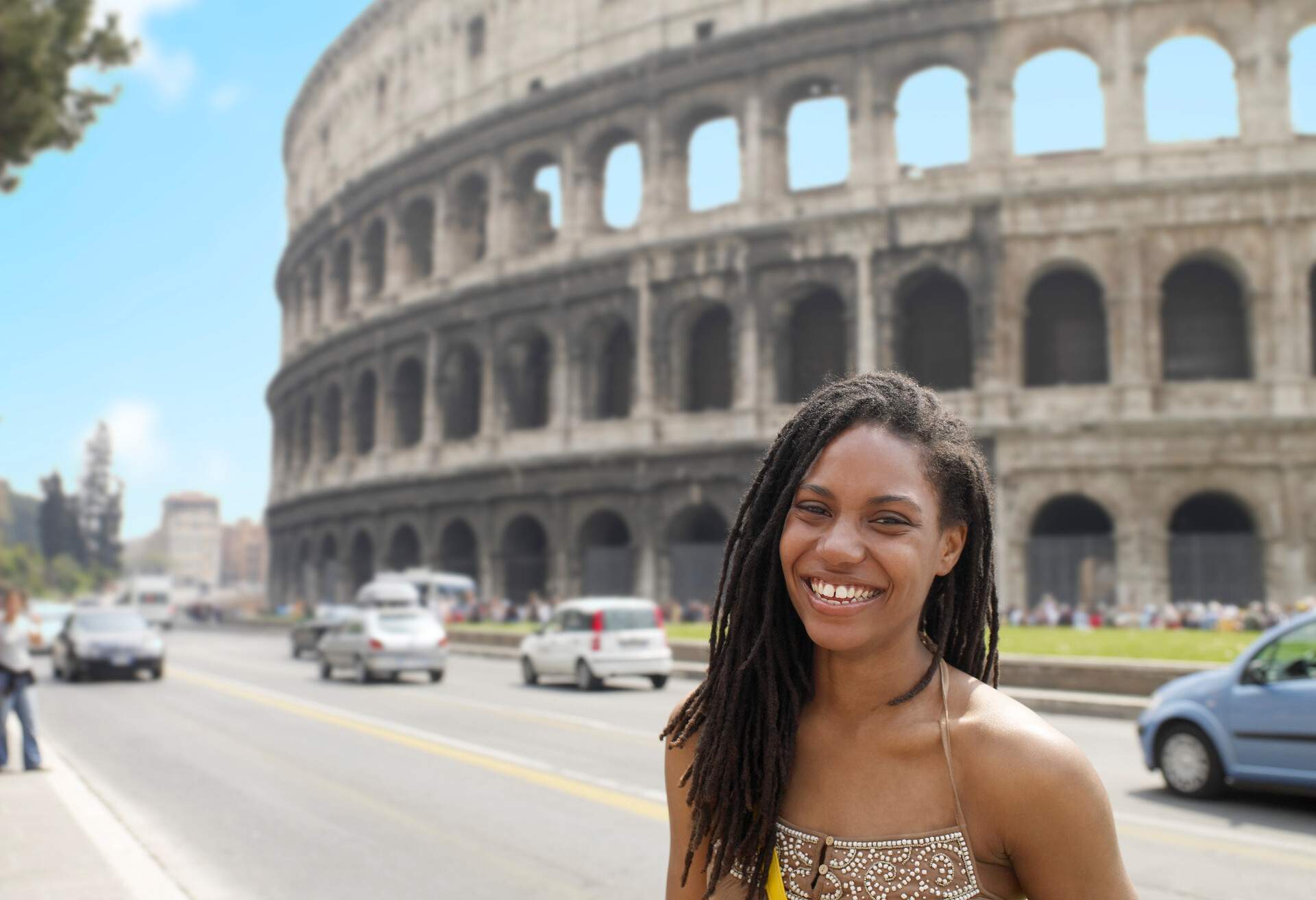 A young lady smiles at the camera with a background of the external arch walls of the ancient Colosseum.