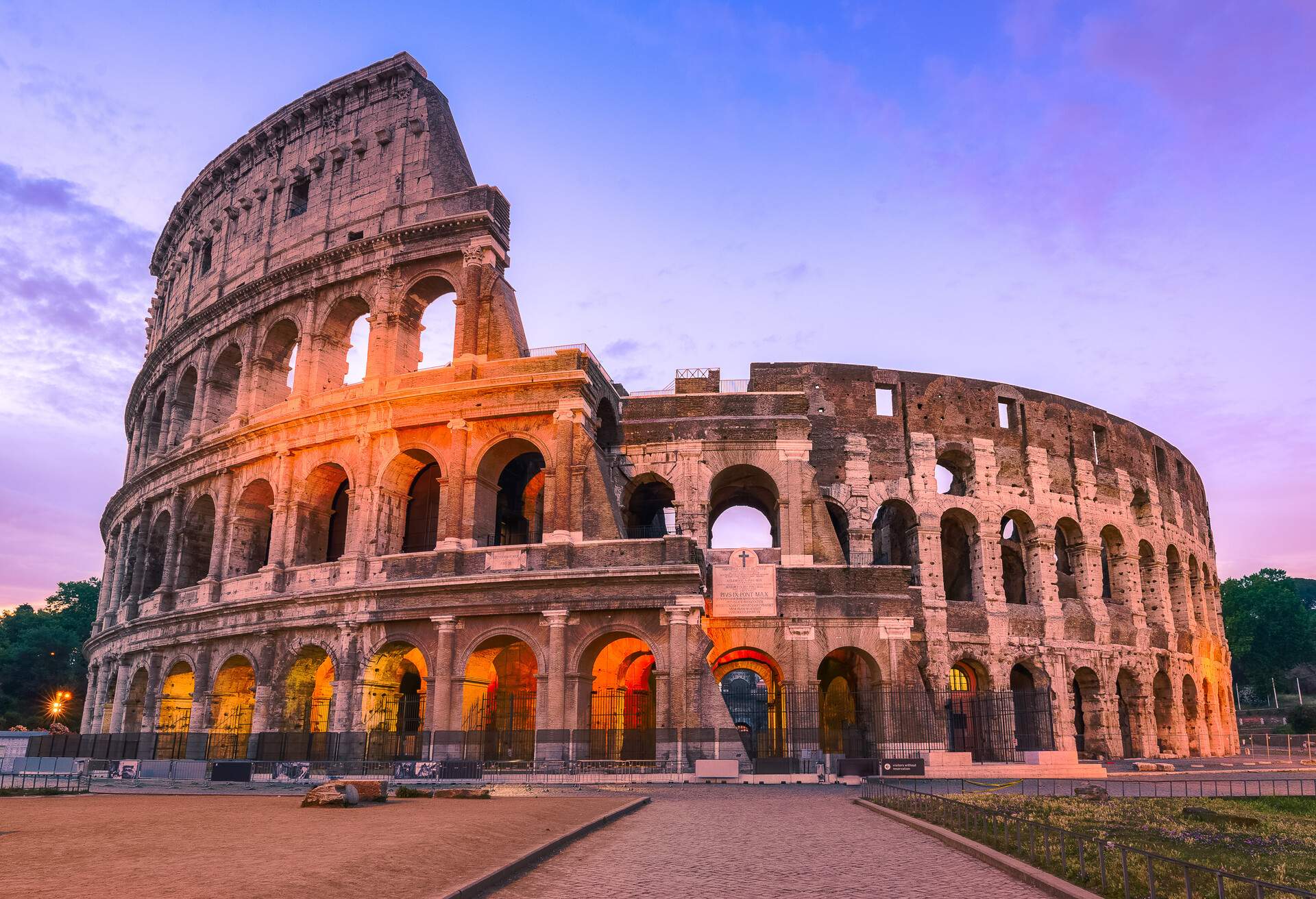 A partially lighted Colosseum against a colourful sky at dusk.