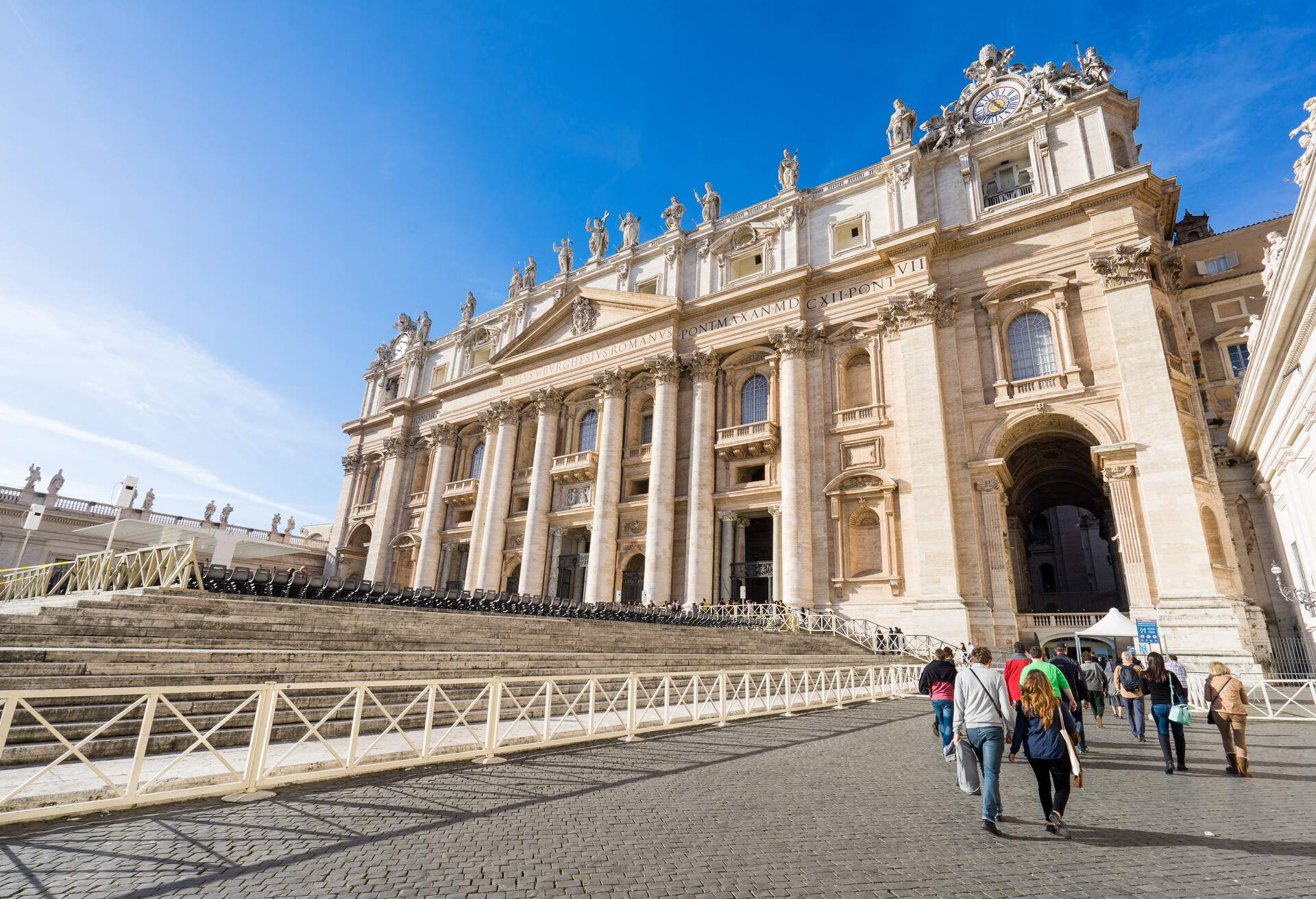 People walking along the bottom of the steps in front of St. Peter's Basilica's main façade