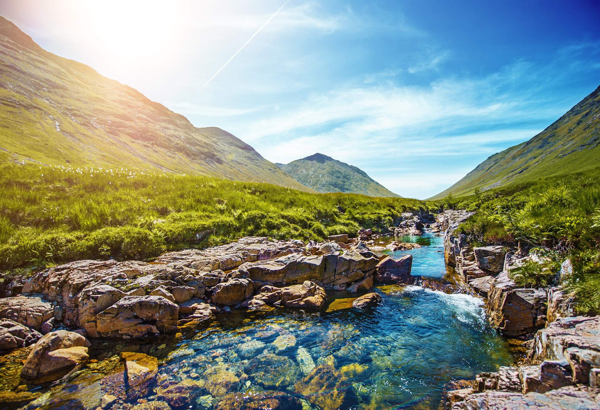 Clear waters flow across a rocky stream between the grassy valleys.