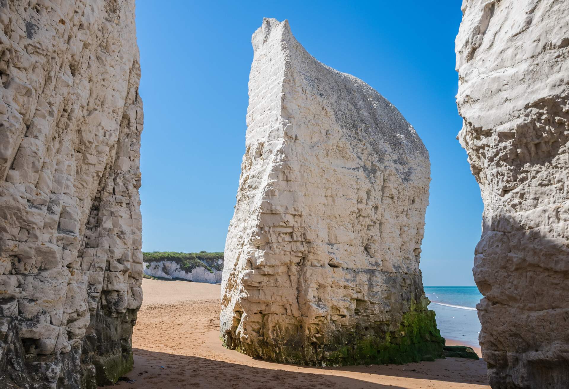 Alongside a turquoise bay surrounded by chalk cliffs are steep vertical rock stacks on golden sands.
