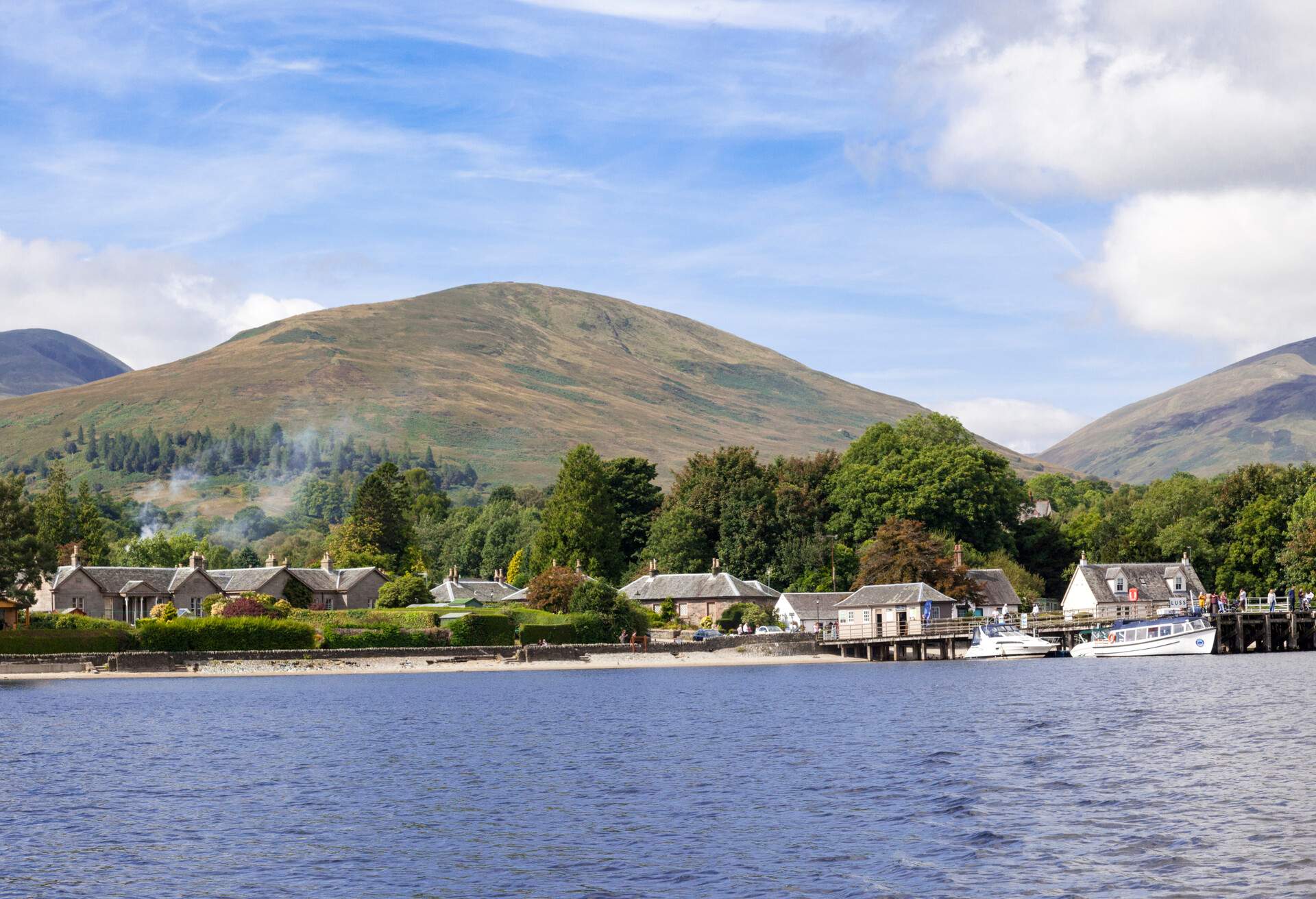 Waterfront cottages and trees along the foothills of massive mountains.