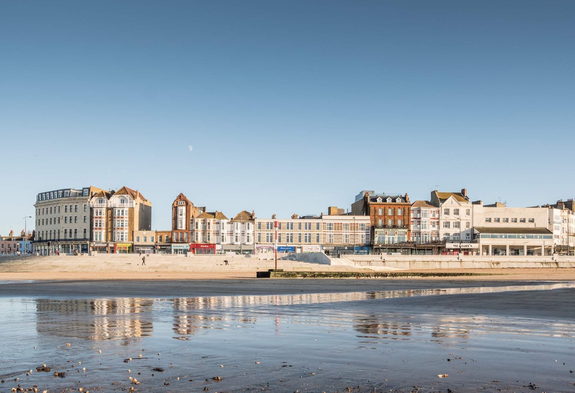 A shore of a beach by the shoal lined with classic and modern buildings against the clear blue sky.