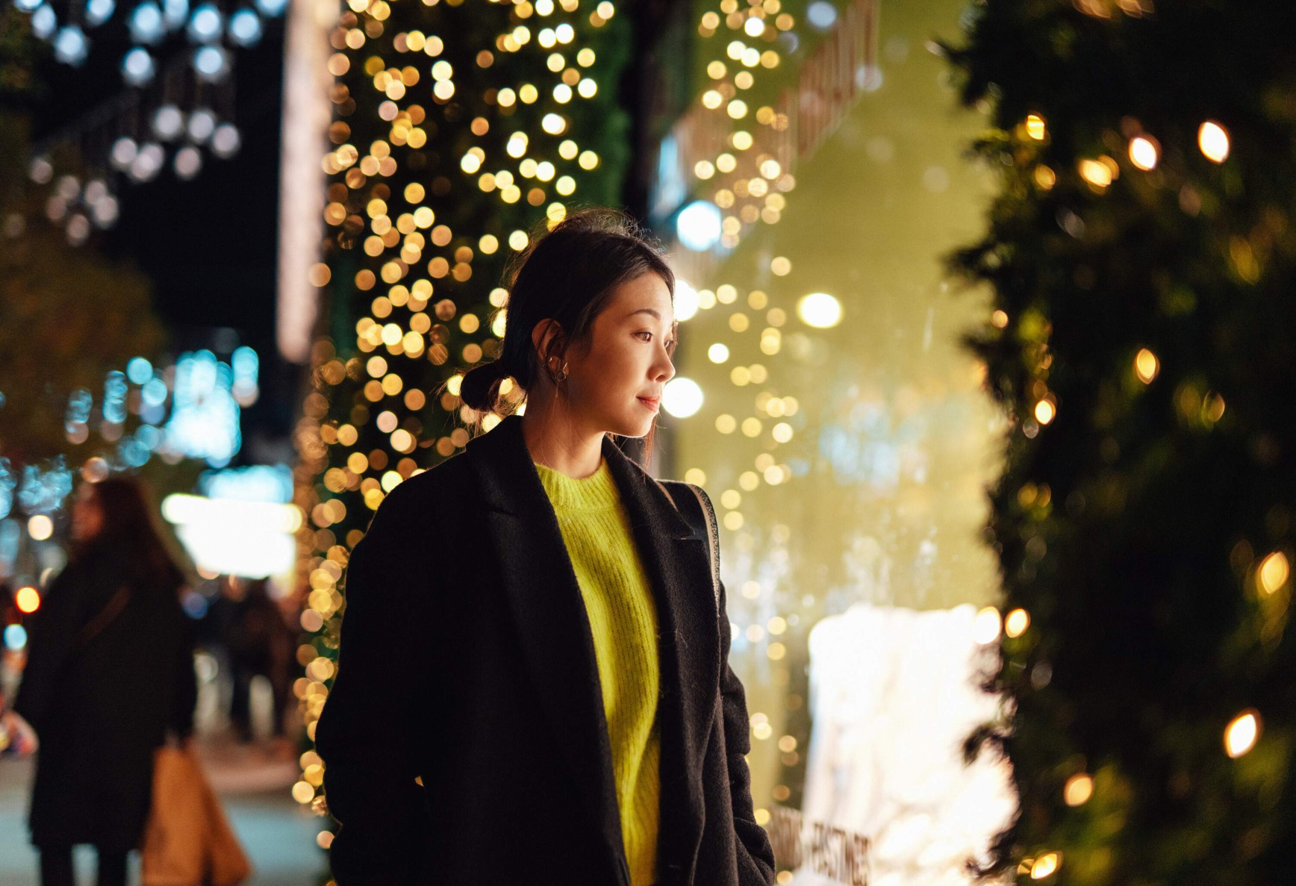 Beautiful young Asian woman look through shop window at night, with illuminated fairy lights in the background. Christmas shopping.