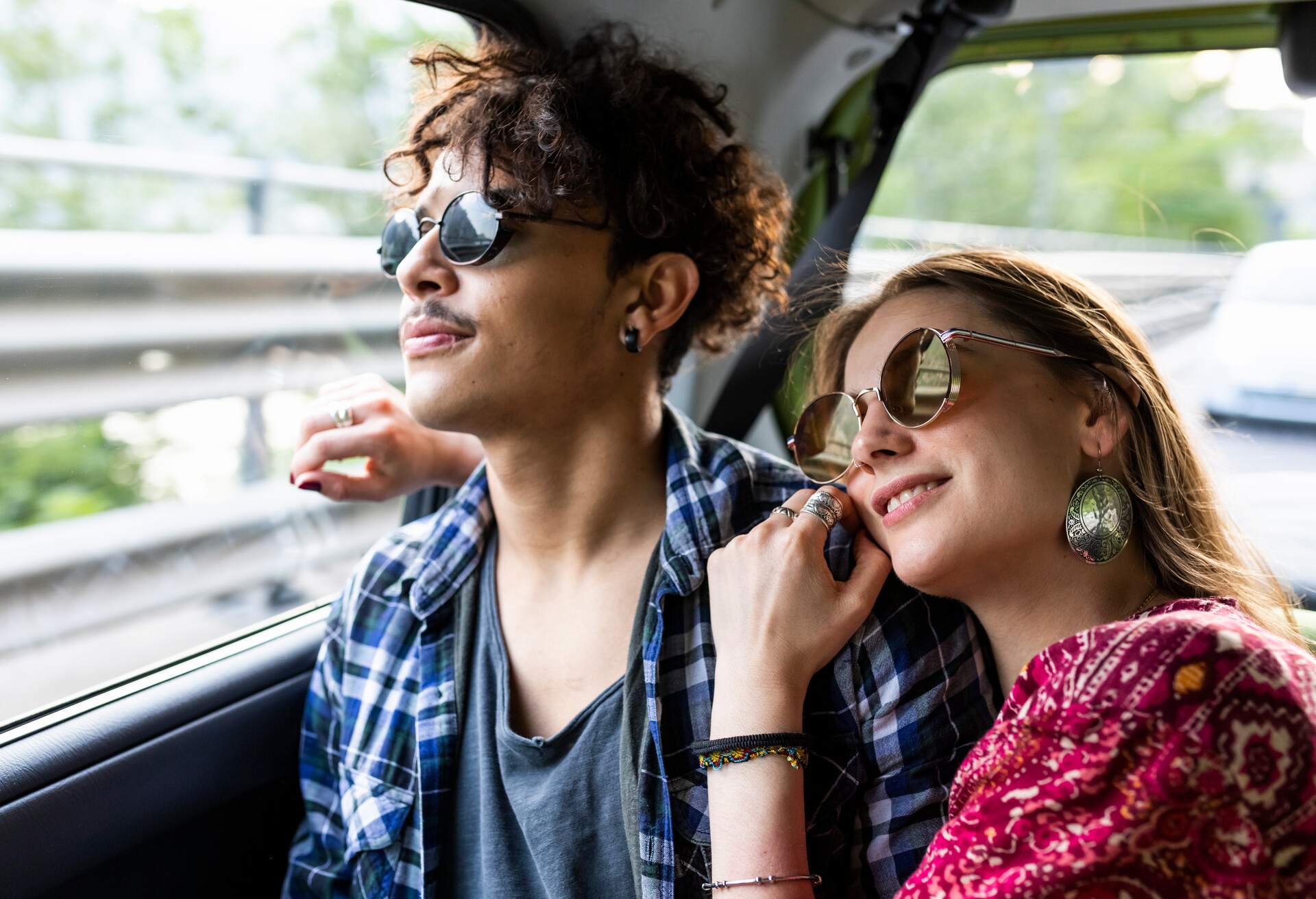 A sweet young couple wearing sunglasses rides on a Uber cab.