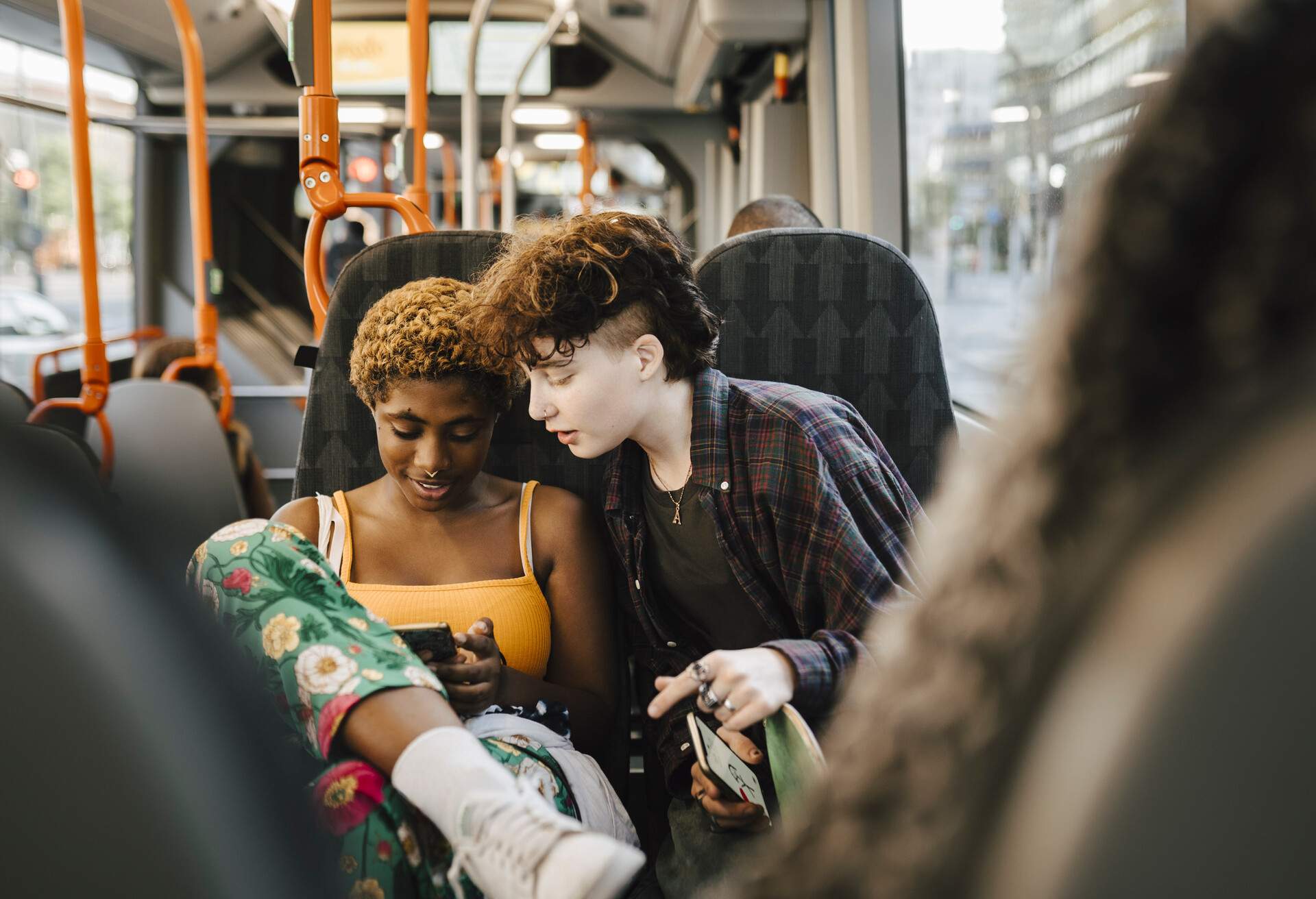 A young man and woman riding on a bus, each holding their smartphone.