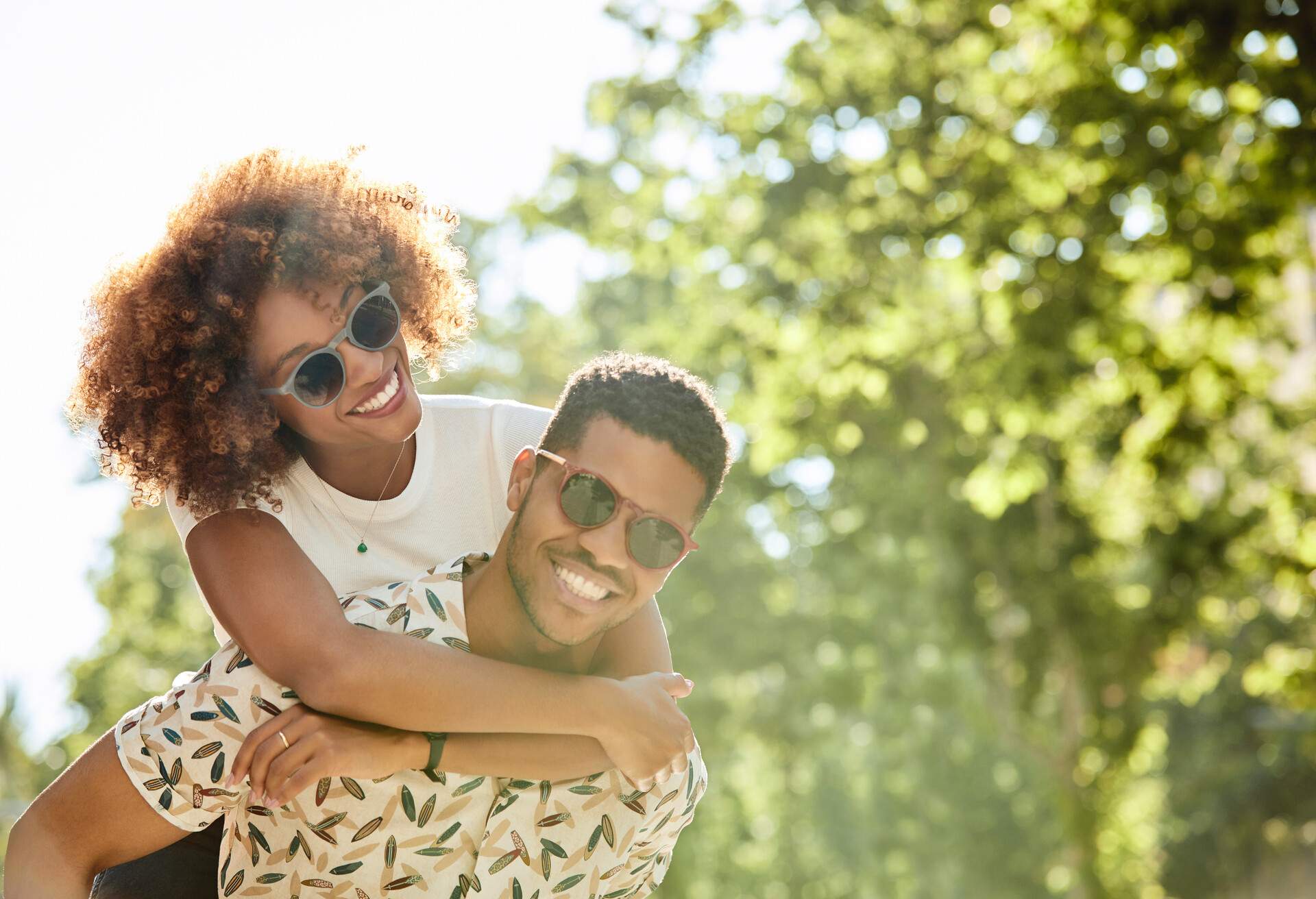 A lovely couple wearing sunglasses on a sunny day on a piggyback ride along the lush plants.