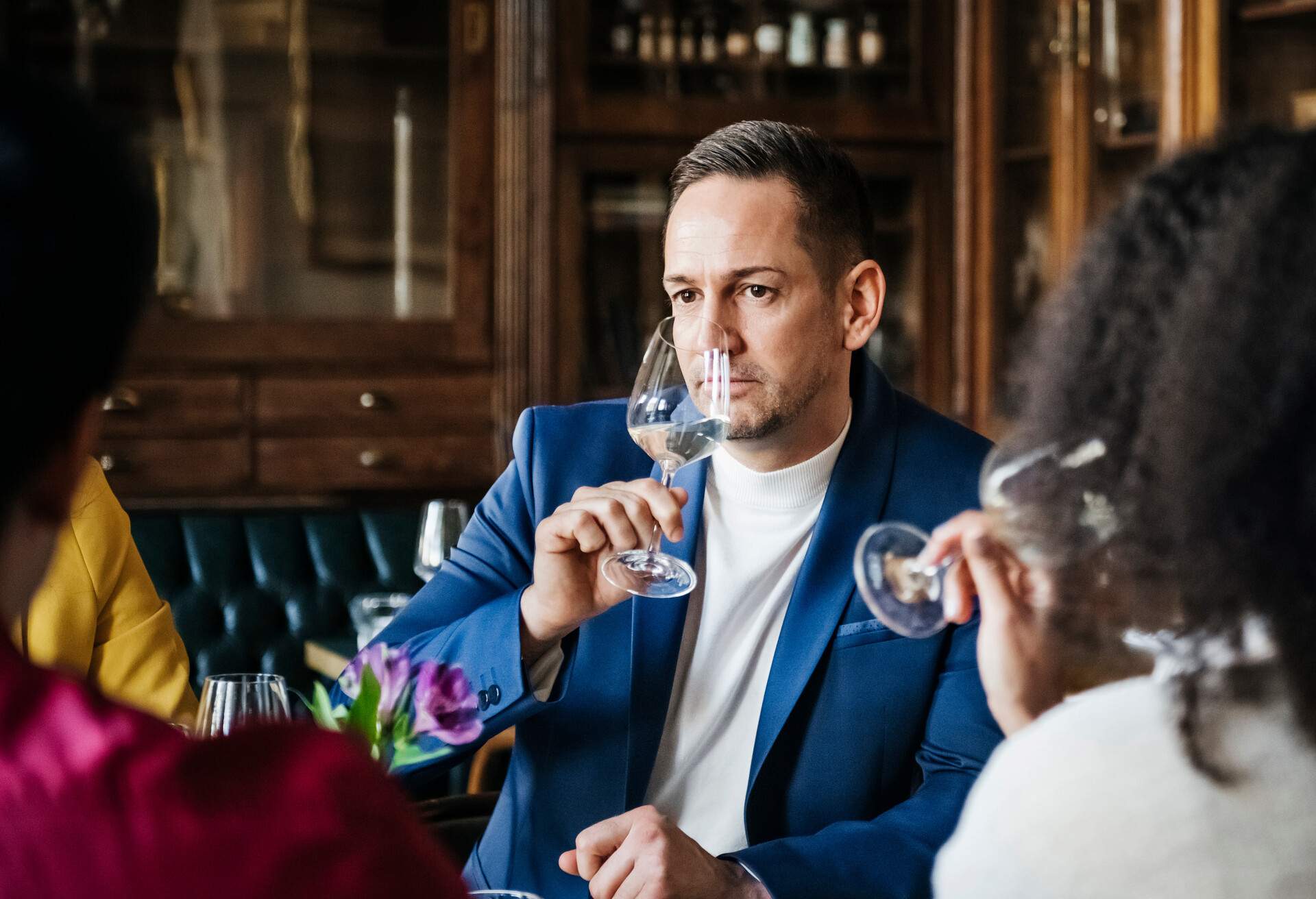 A man in a blue blazer inhaling the intoxicating scent of wine before drinking.