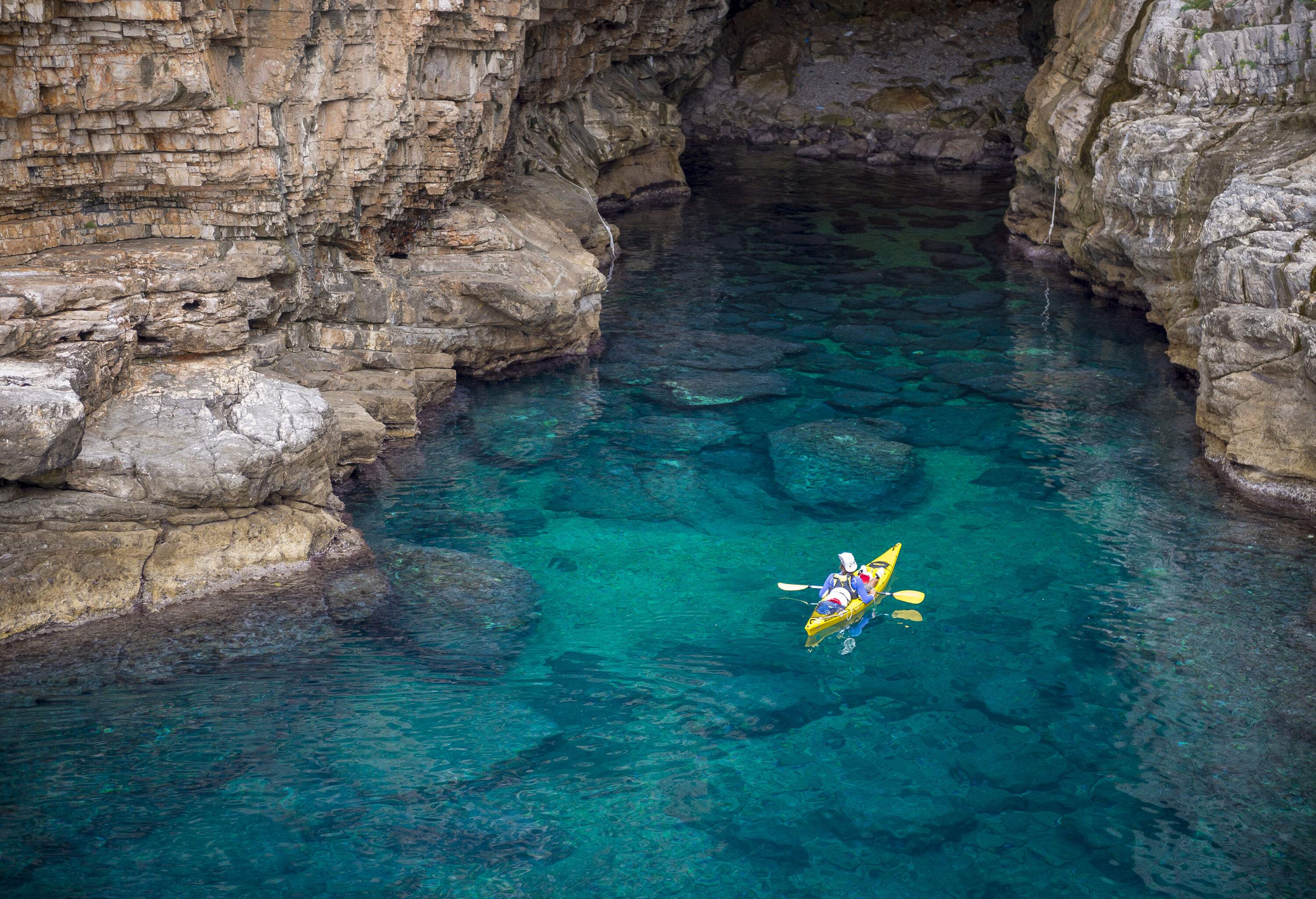 A kayaker glides away on tranquil waters, surrounded by majestic rock cliffs and crystal-clear views.