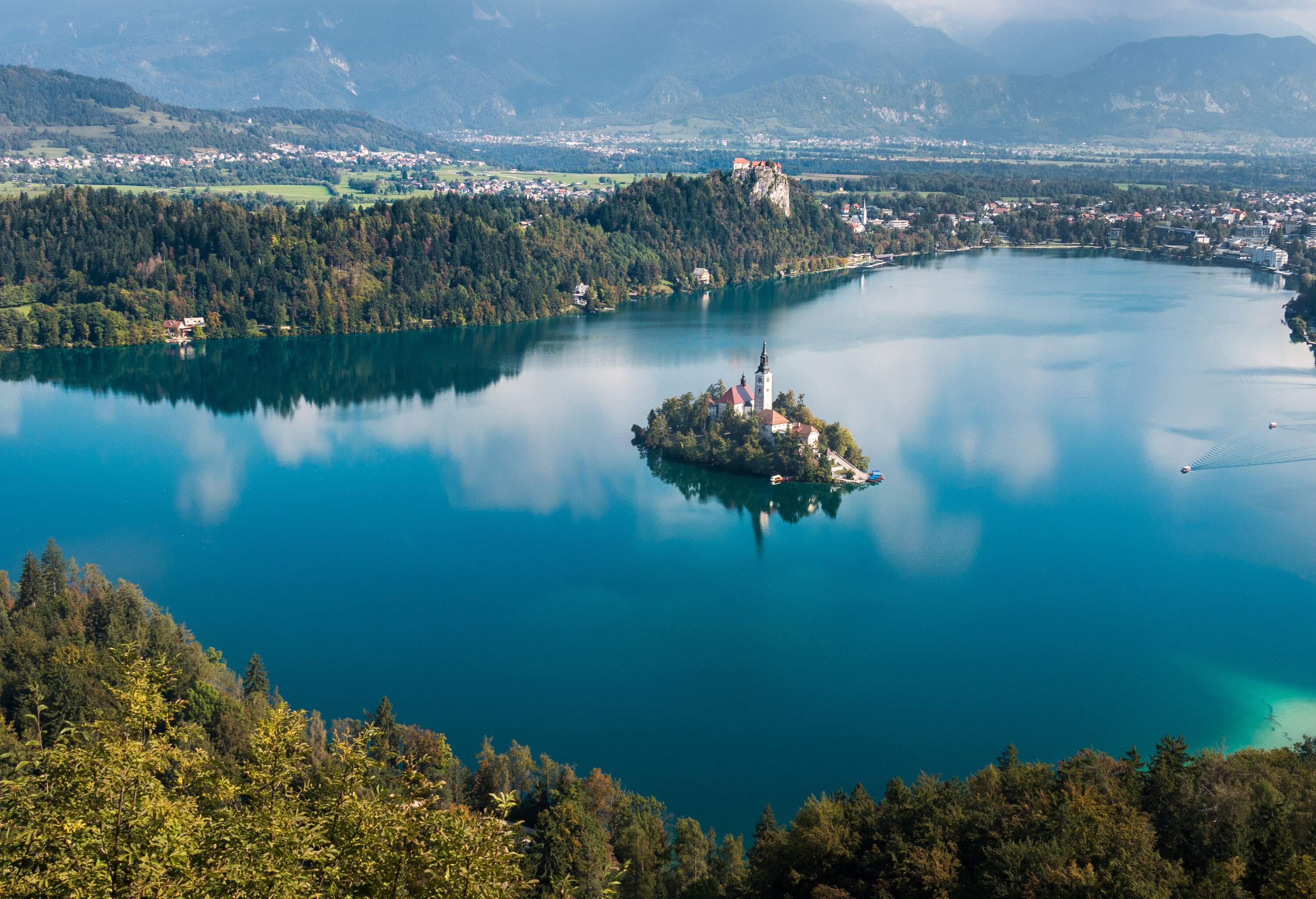 A townscape and dense forest surround a lake that has an island church in the middle.