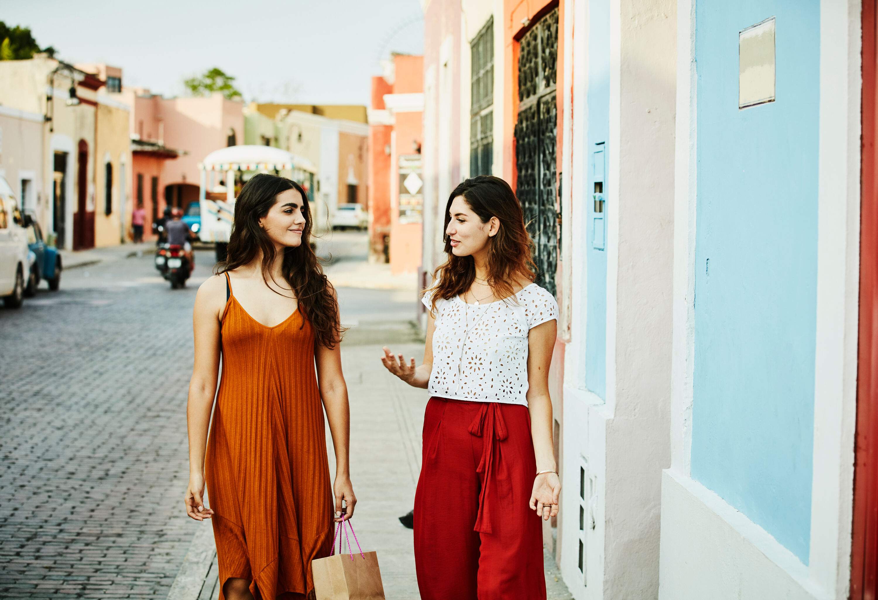 Two female friends chatting as they go along the sidewalk.