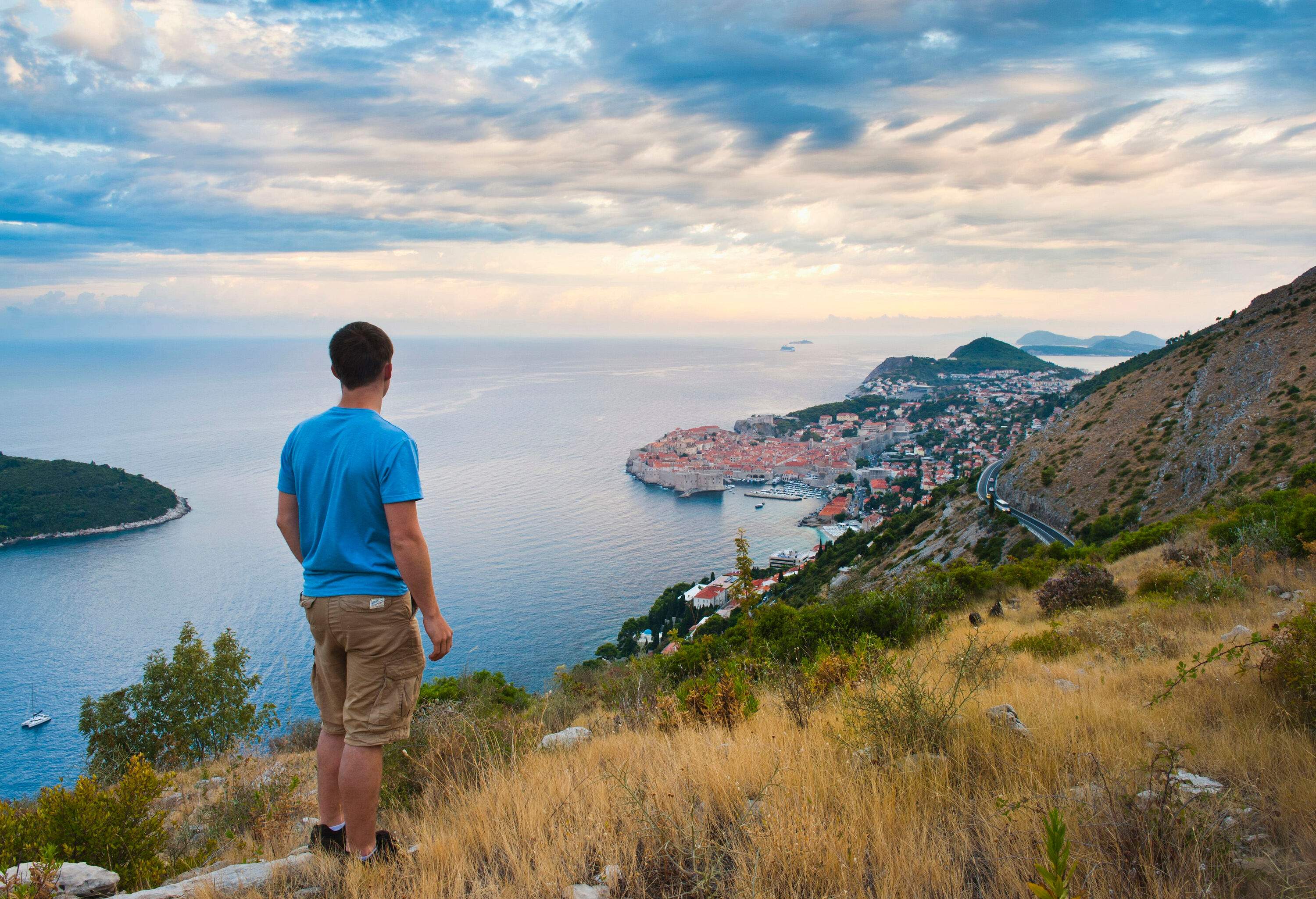 A man standing on the hillside and admiring the view of the sea and the city below.