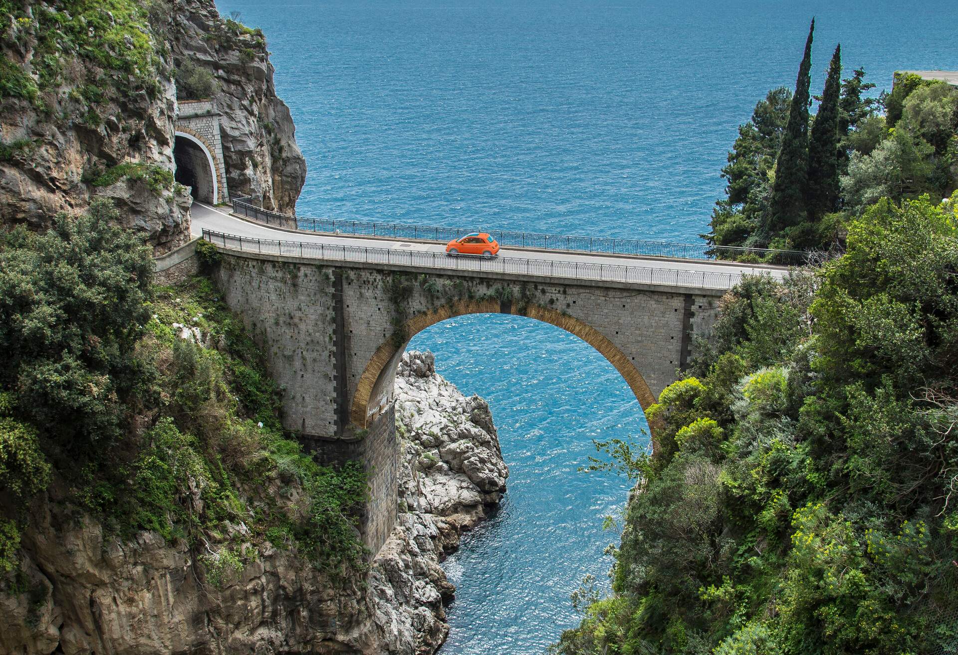 A car crosses a seaside gorge on an arch bridge.