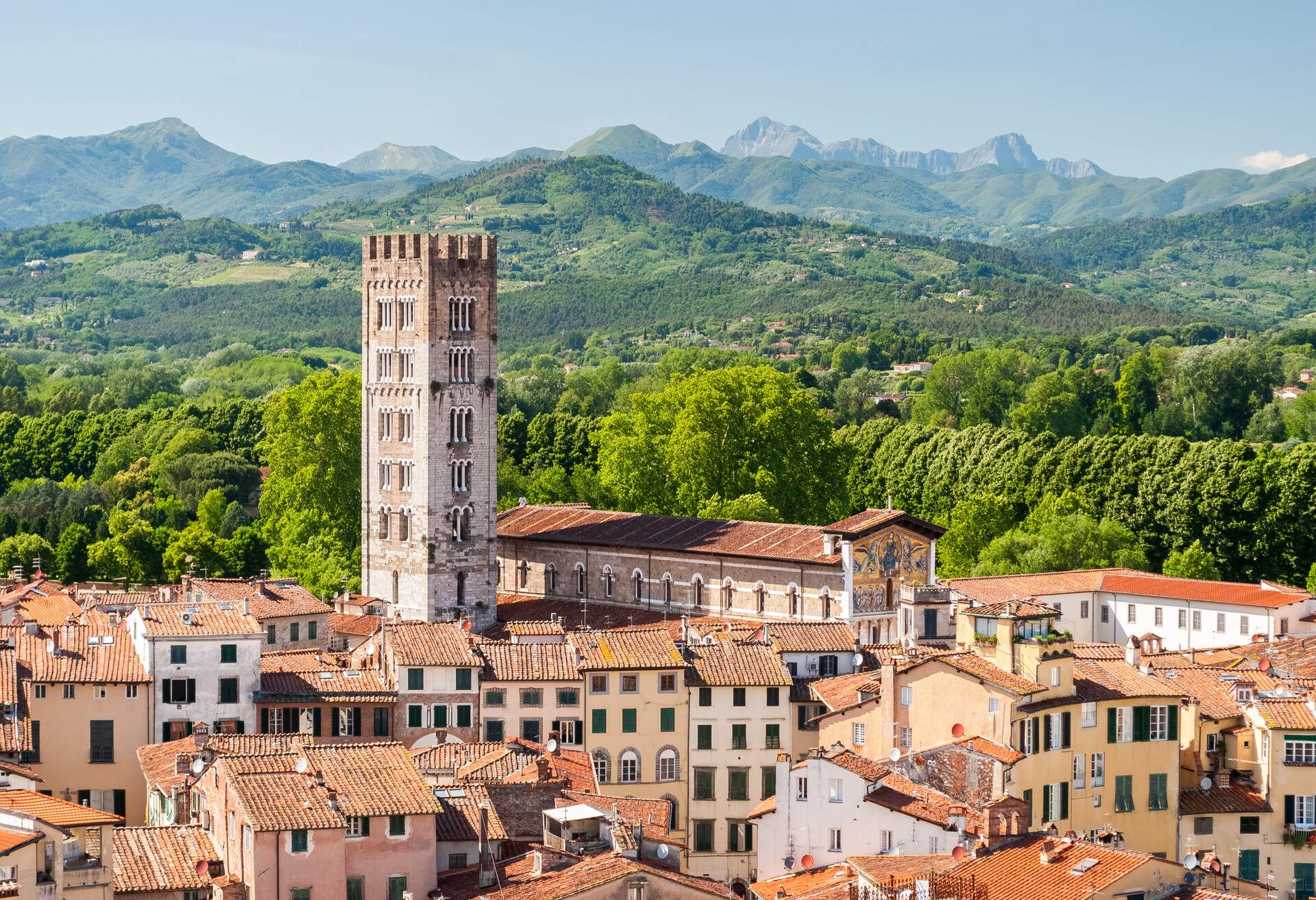 A tower dominates a cluster of compact houses surrounded by lush trees and forested mountains.